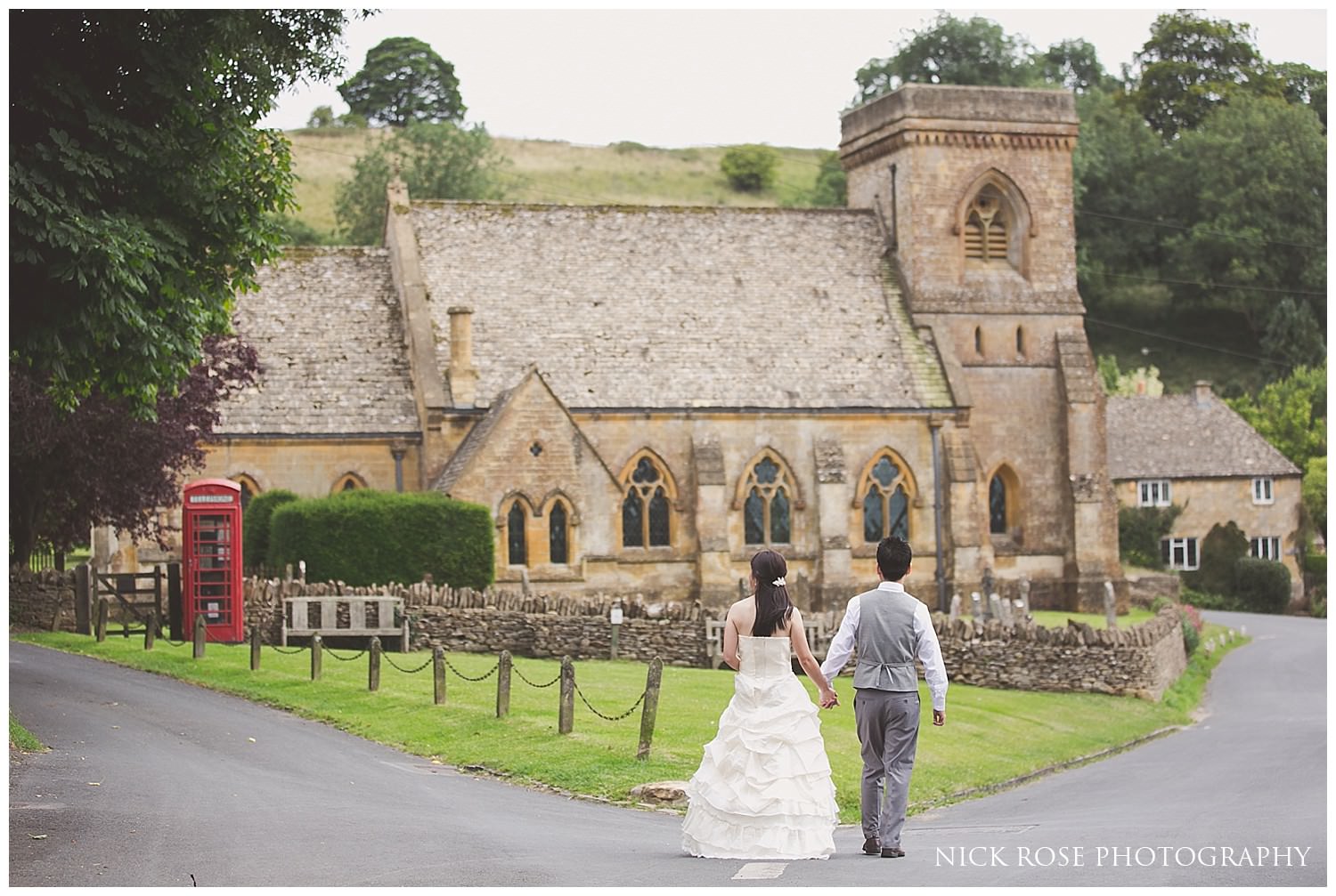  Pre wedding photograph of a couple walking towards and church and red phone box in the cotswolds 