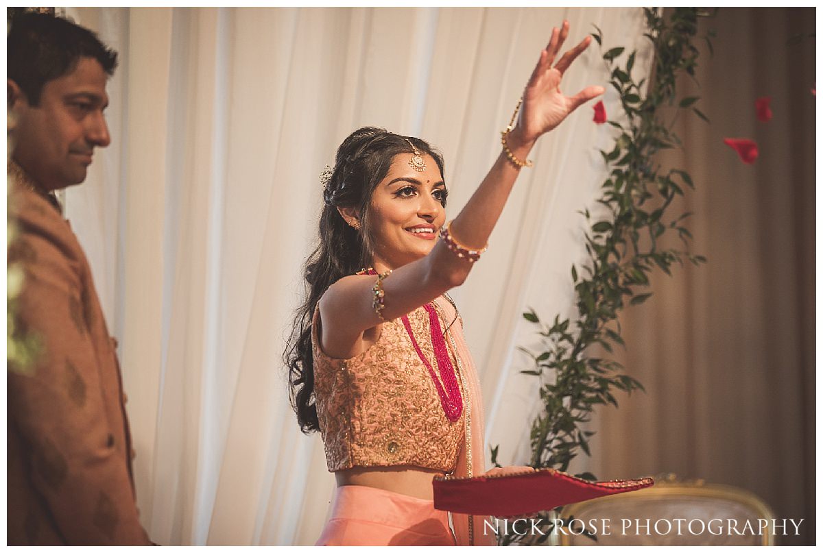 Bridesmaid throwing flowers as the bride and groom walk around the fire during a Hindu wedding in Hertfordshire