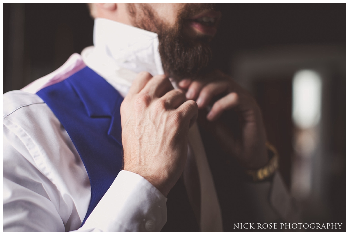  Groom putting on tie before a Buxted Park hotel wedding in East Sussex 