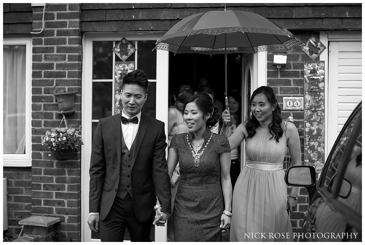  Bride and groom leaving house under a red umbrella before their London Chinese wedding 