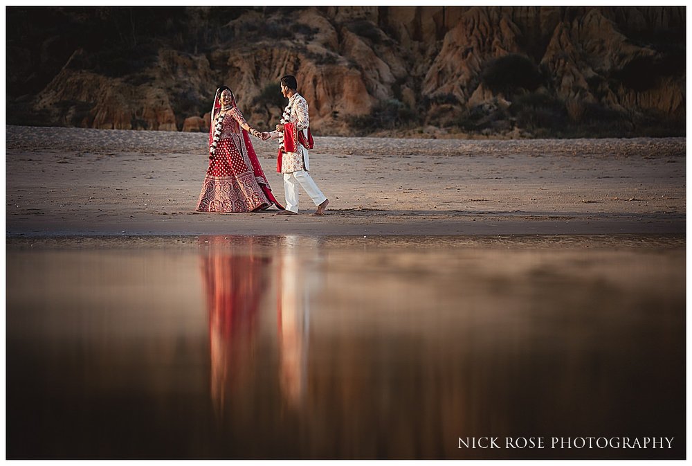  A beautiful image of the bride and groom holding hands, walking on the sandy beach at the Pine Cliffs resort in Portugal for a destination Hindu wedding photographed by destination wedding photographer Nick Rose 