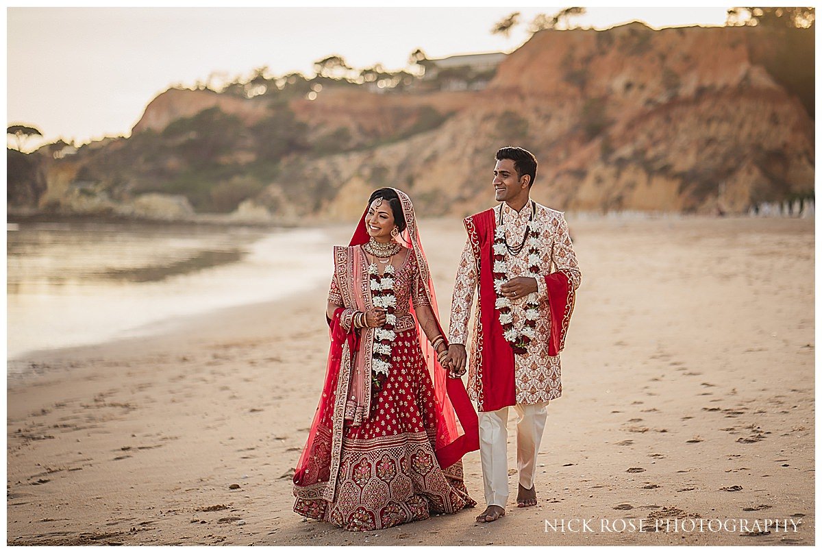  The newlyweds holding hands and walking along the shoreline at Pine Cliffs Resort, with the ocean and cliffs in the background, captured by destination wedding photographer Nick Rose 