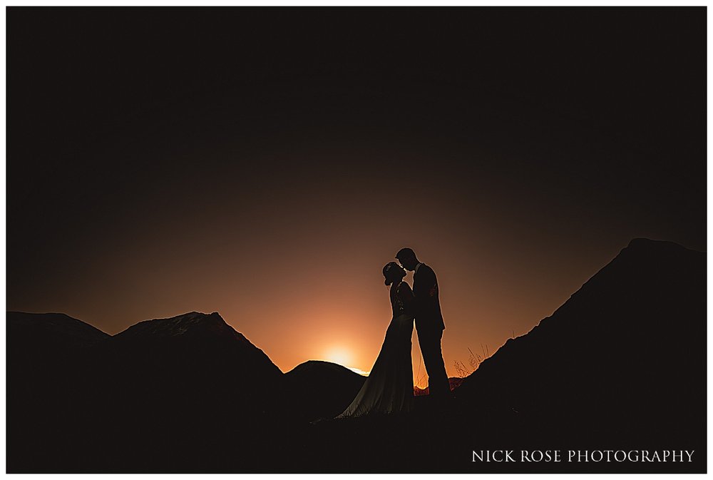  A romantic sunset shot of a couple embracing on a hillside in Glencoe, surrounded by mountains. 