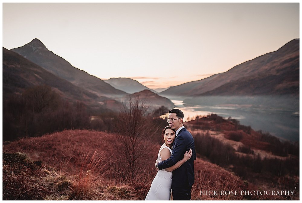  A couple standing by a Scottish loch taking in the panoramic view of Glencoe's valleys and hills. 