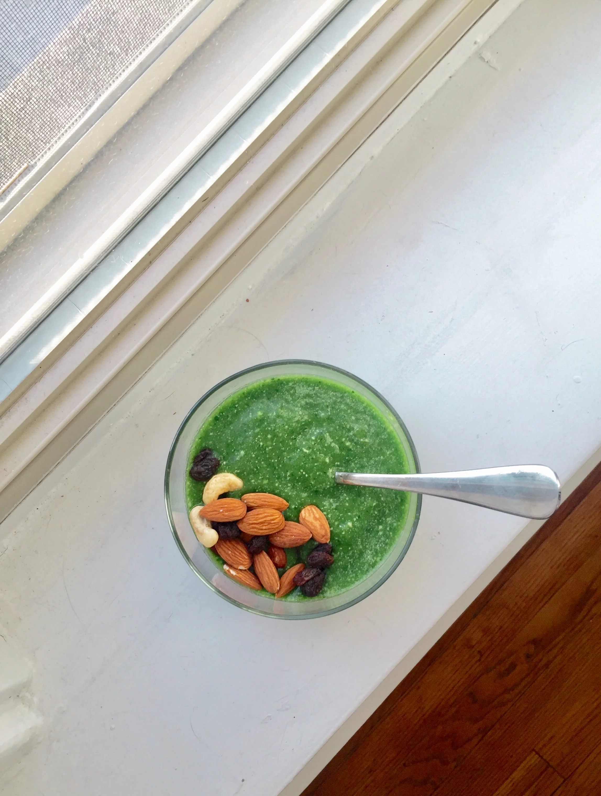 Banana + spinach + cashew milk smoothie bowl topped with cashews and almonds and raisins