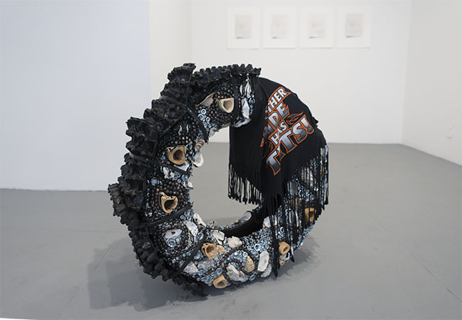   A.K. Burns &amp; Katherine Hubbard,   In spirit of (the new misandry) , 2014. Tire, bones, wooden beads, oyster shells, bolts, cardboard egg crates, rubber bungee cords, cement rock, enamel, t-shirt. 