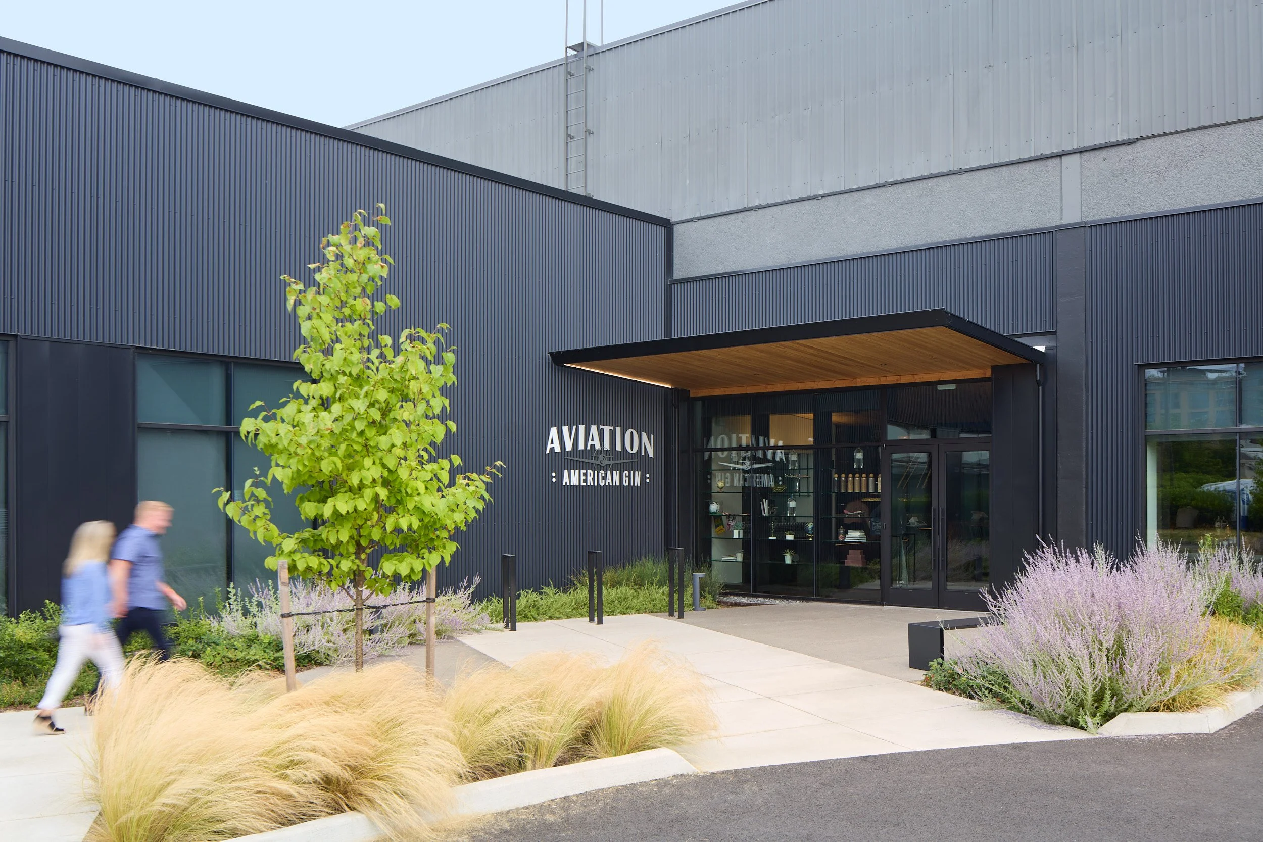 Exterior architectural detail image showing customers approaching the Aviation Gin Distillery entrance, with lush landscape design, designed by fi architecture, in Portland, Oregon.