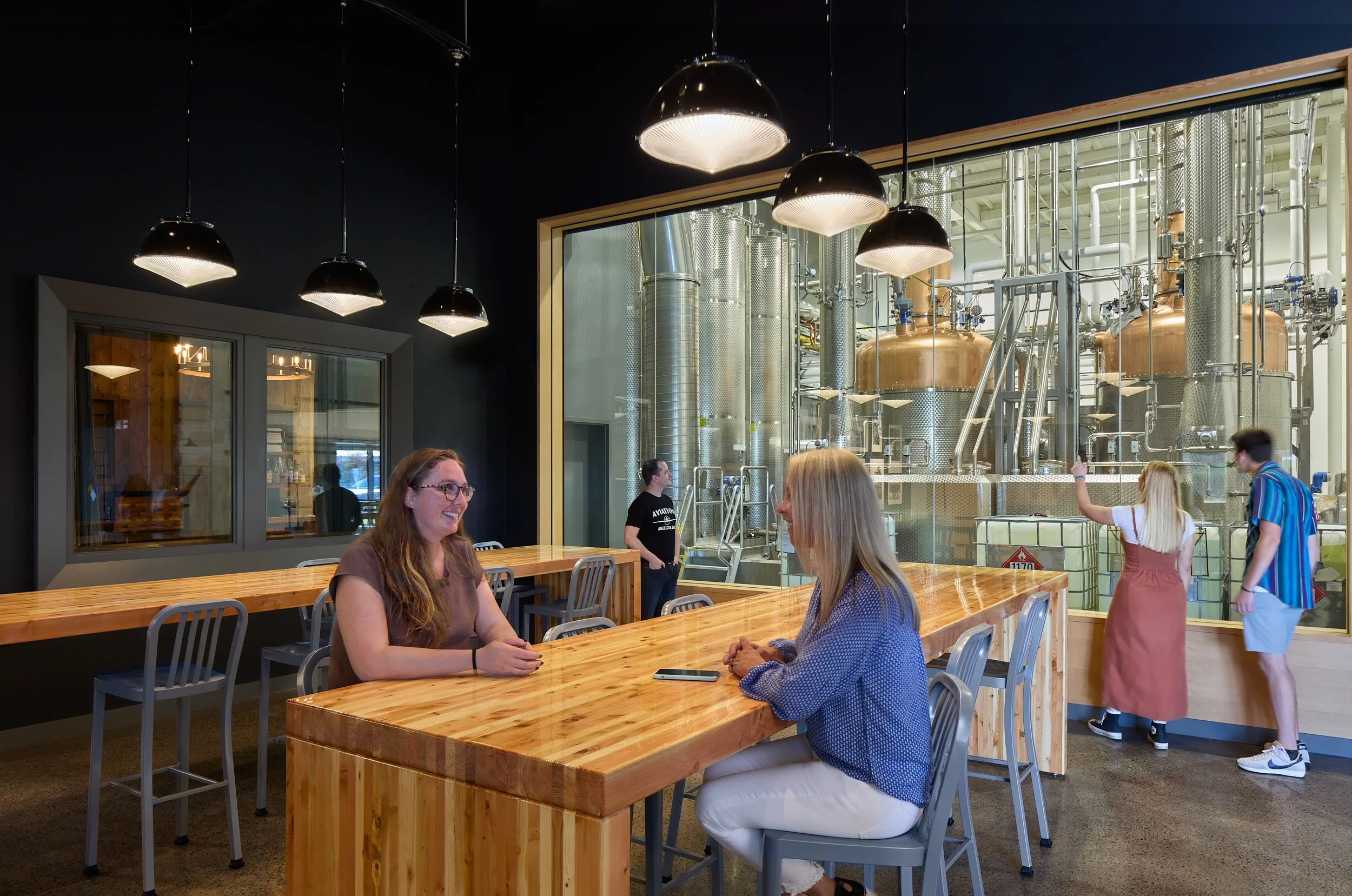 Interior lifestyle photograph showing patrons seated in the Aviation Gin Distillery tasting room and visitor experience area in Portland, Oregon, designed by fi architecture.