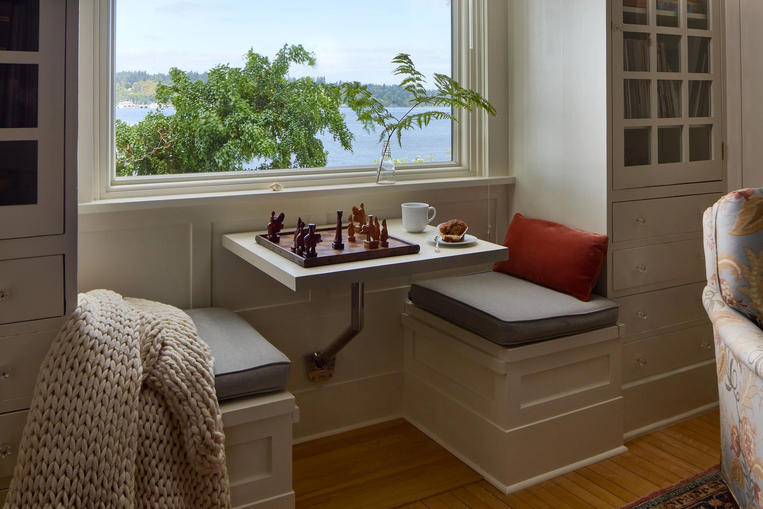 Cozy interior photo of a window nook featuring a custom bench and built-in shelving, with a chess set on the table, Olympia, WA, designed by Brown Building Contractors.