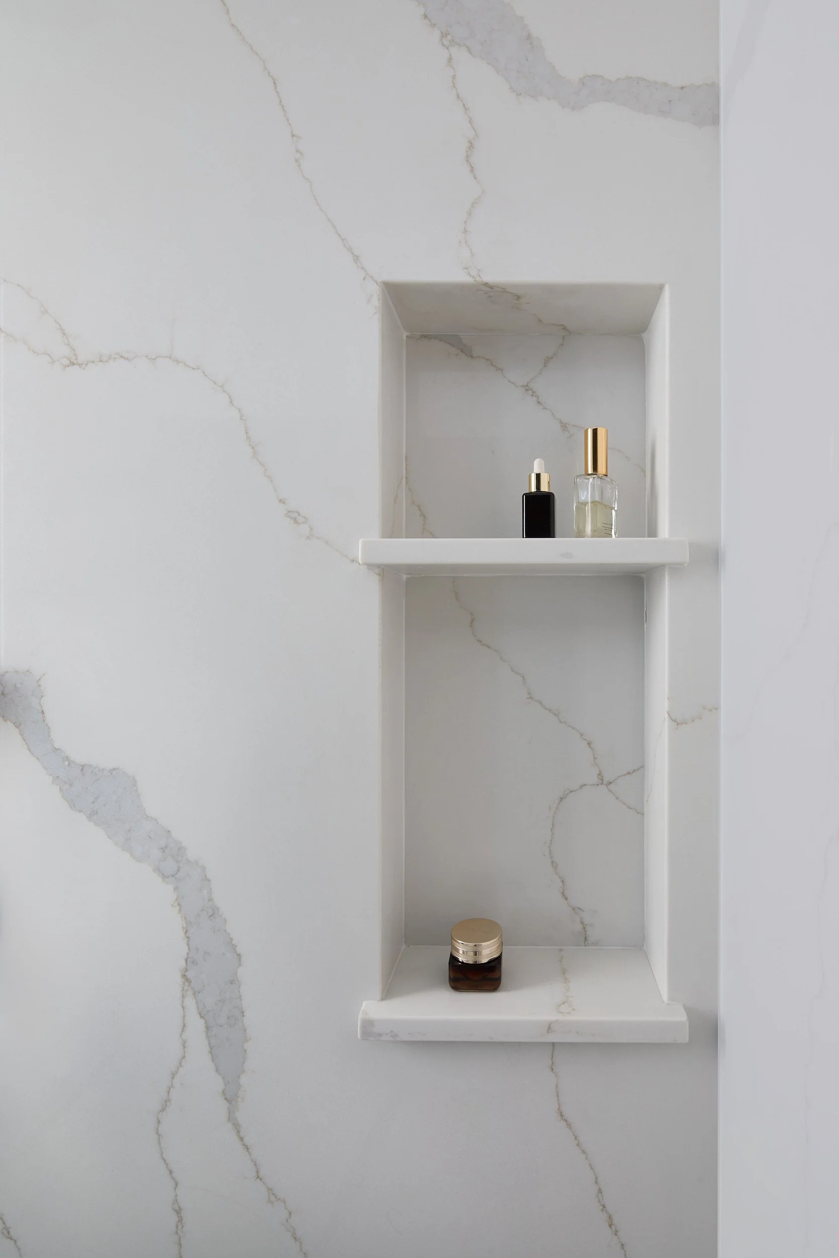 Tight view of a custom marble shower area in an Eastside Olympia Residence, highlighting a built-in shower niche and high-end glass door, built by Brown Building Contractors.