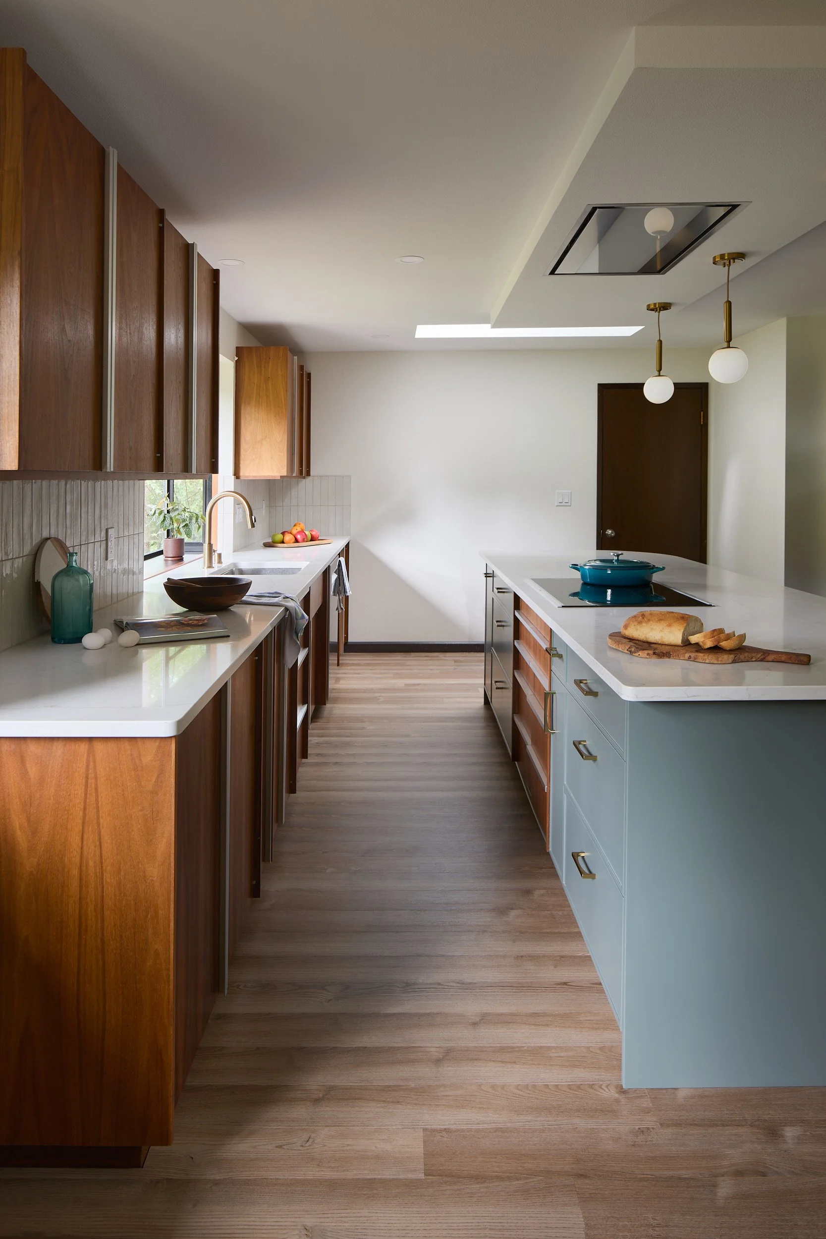 MCM galley kitchen in Olympia, WA, featuring original wood cabinets, soft blue-green island, built-in appliances, and custom lighting by Brown Building Contractors.