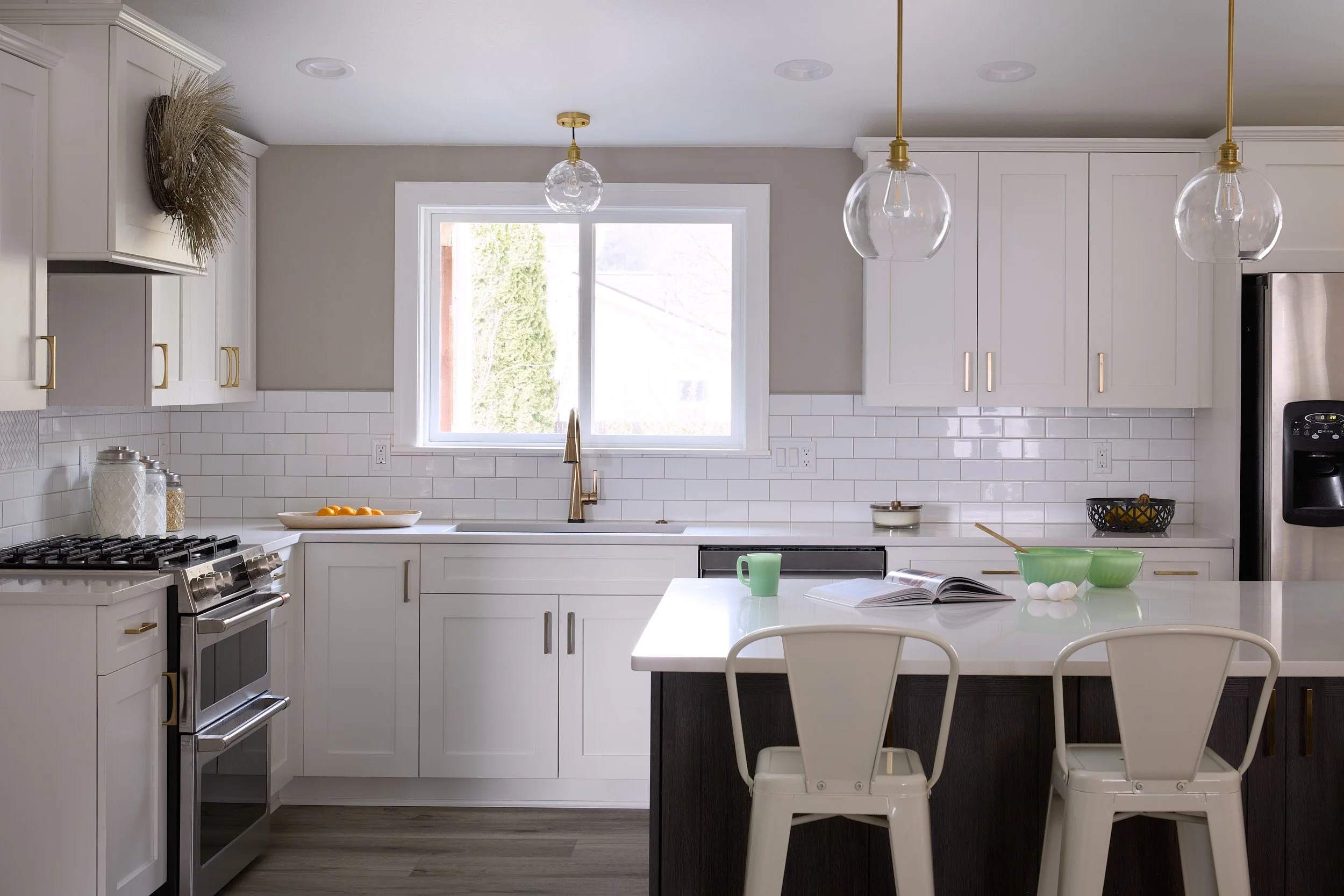 All-white kitchen remodel in Olympia, WA, featuring a large island with black satin paint, bold gold fixtures, and quartz countertops by Brown Building Contractors.
