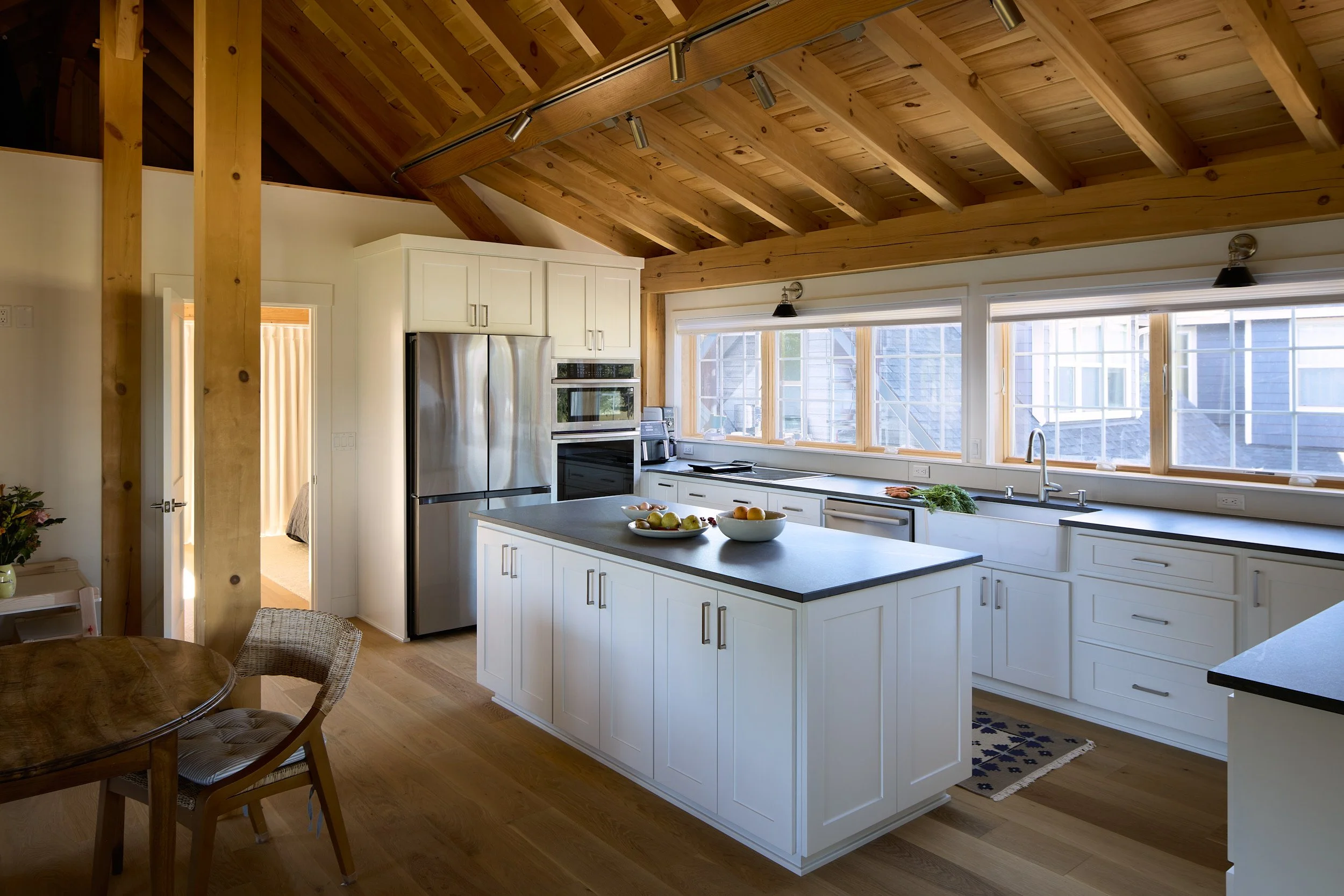 Interior photo of the Rangeley Timber Frame Barn Home kitchen in Ridgefield, WA, featuring exposed timber beams, wooden ceilings and floors, custom cabinetry, and high-end stainless steel appliances.