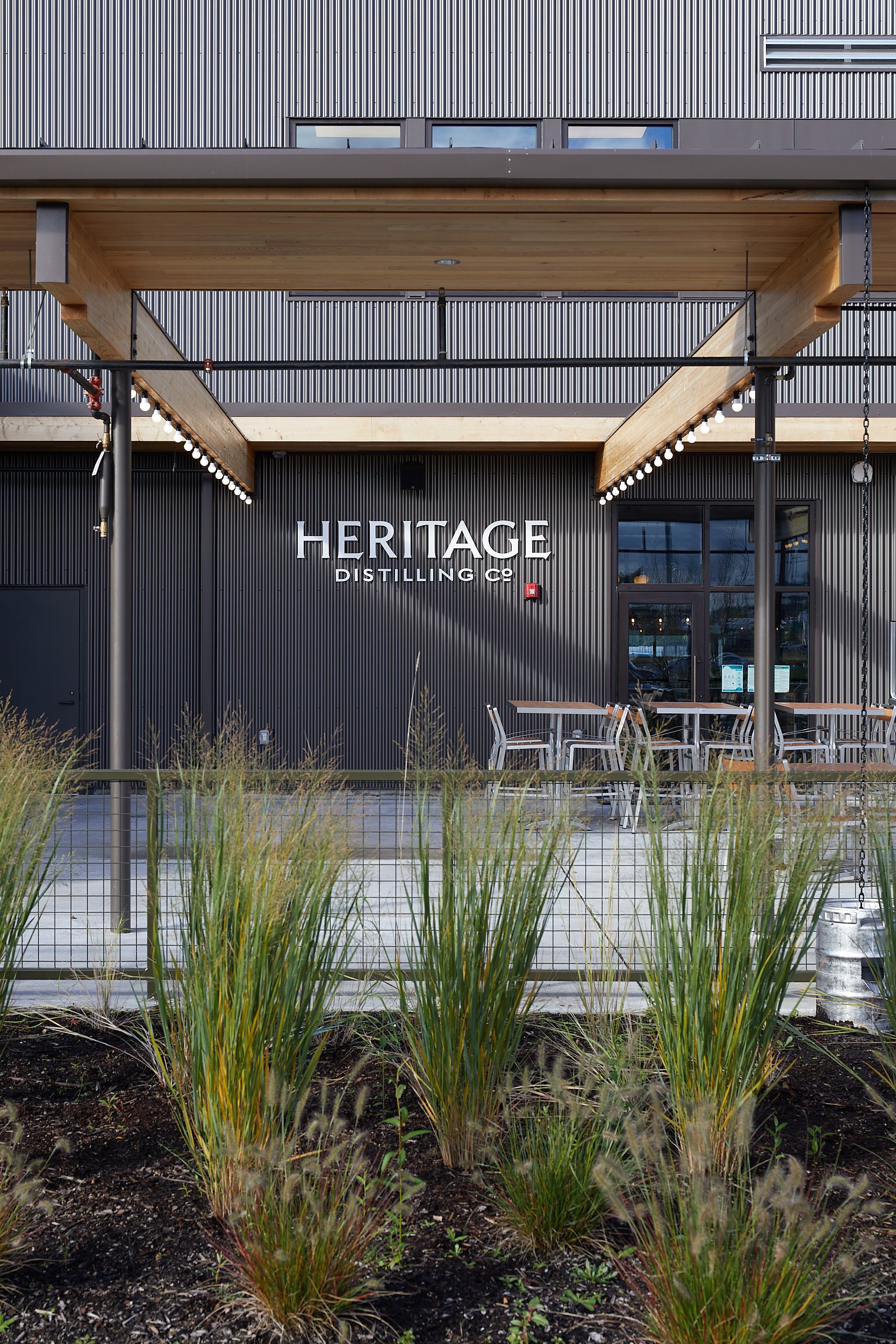 Vertical architectural detail image of the Talking Cedar Brewery and Distillery outdoor seating area, showcasing landscape foliage and exterior design, in Grand Mound, Washington, designed by fi archi