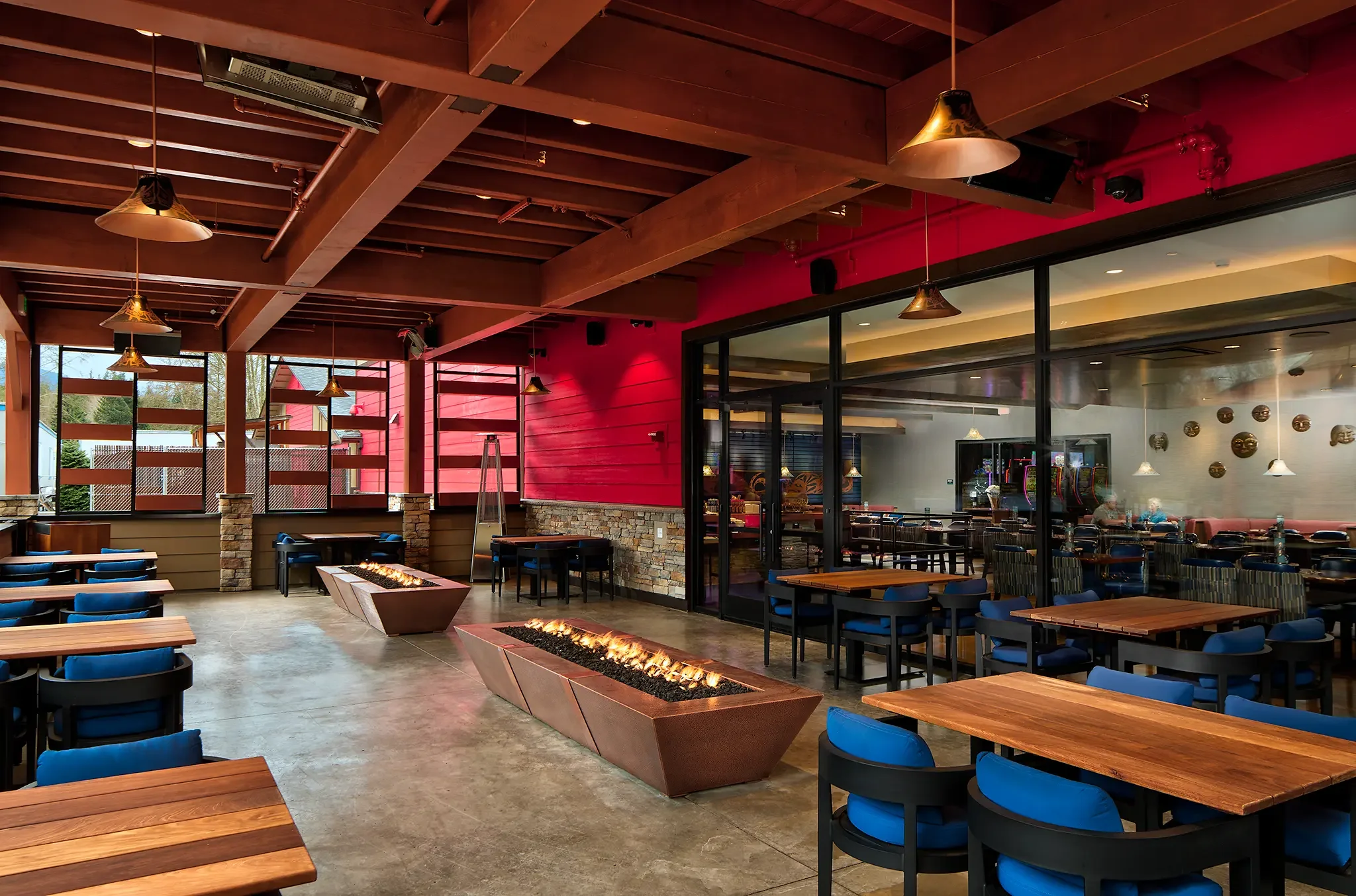 Vibrant red and colorful covered outdoor bar area, connected to the Salish Wind Bar at Elwha River Casino, featuring long illuminated fire pits.