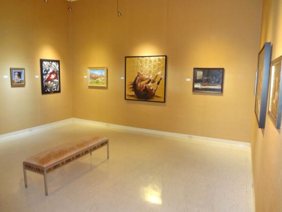 museum room with paintings on the wall and a bench in the center.