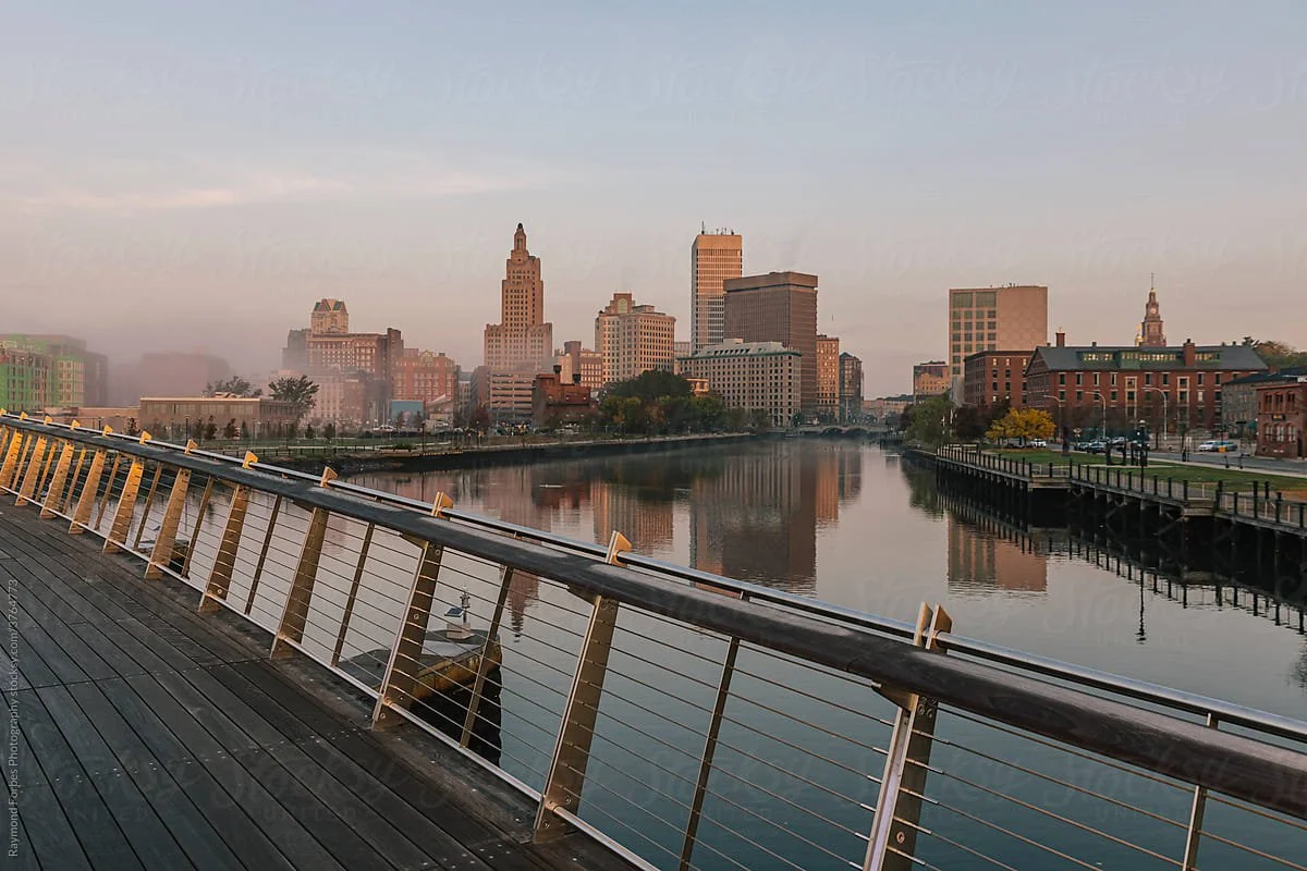 City skyline along a river viewed from a boardwalk at sunrise or sunset.
