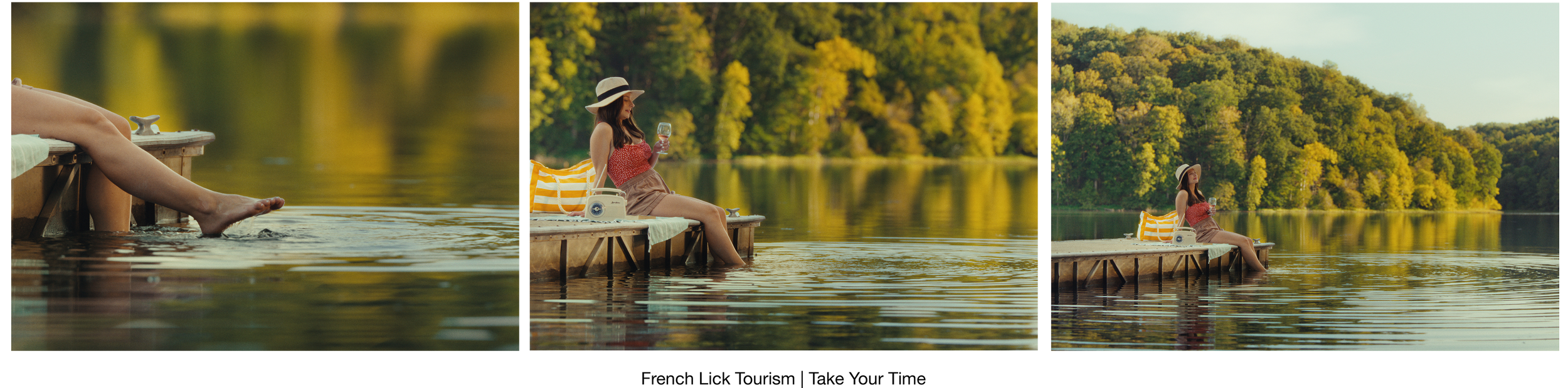 A woman sits on a dock by a lake, wearing a sun hat, holding a glass of wine, with a yellow and white striped bag and a camera beside her. The background features lush green trees and calm water, suggesting a peaceful, scenic outdoor setting.
