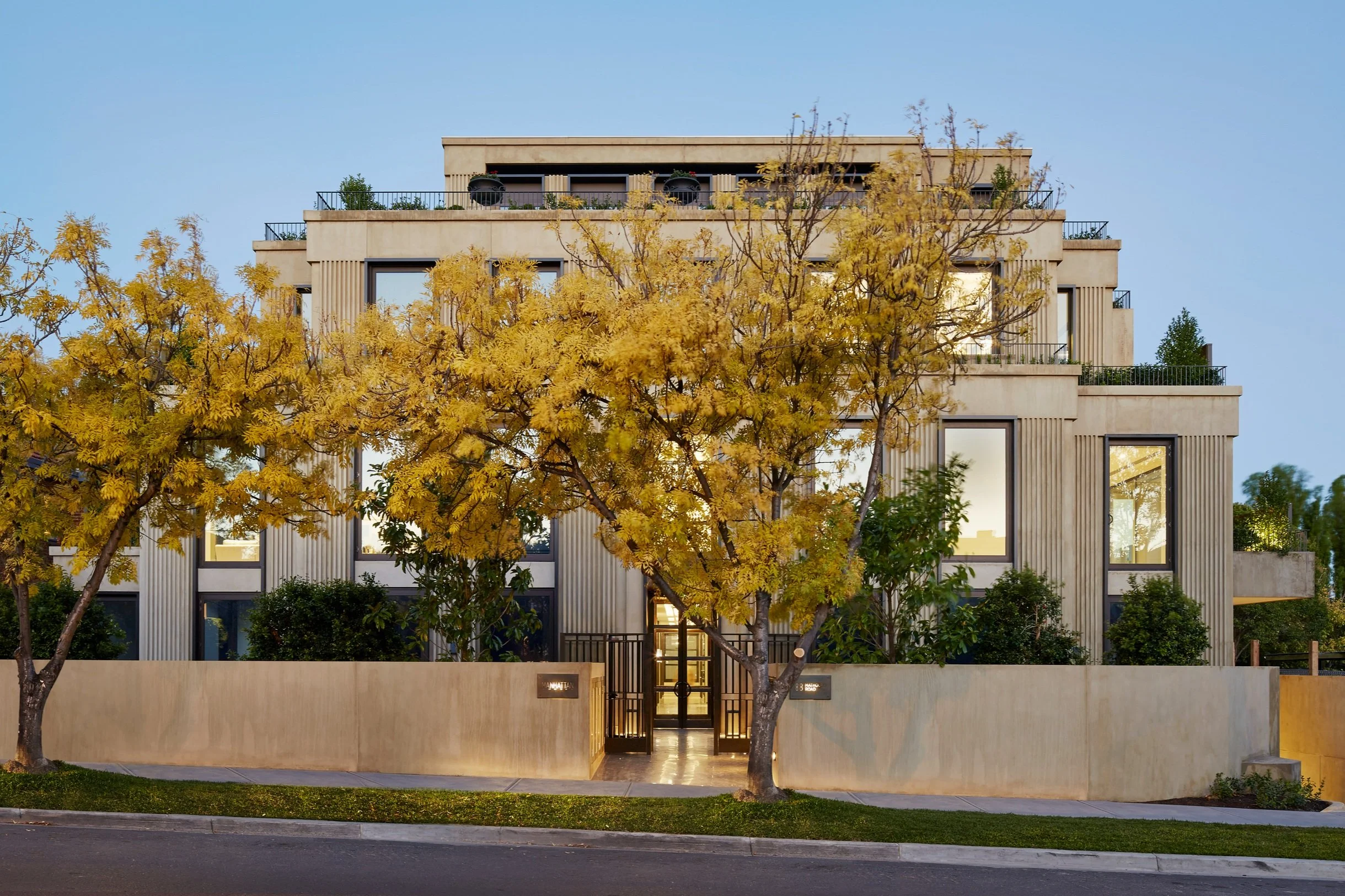 A large four story building is dwarfed by spectacular trees with autumn leaves in yellow