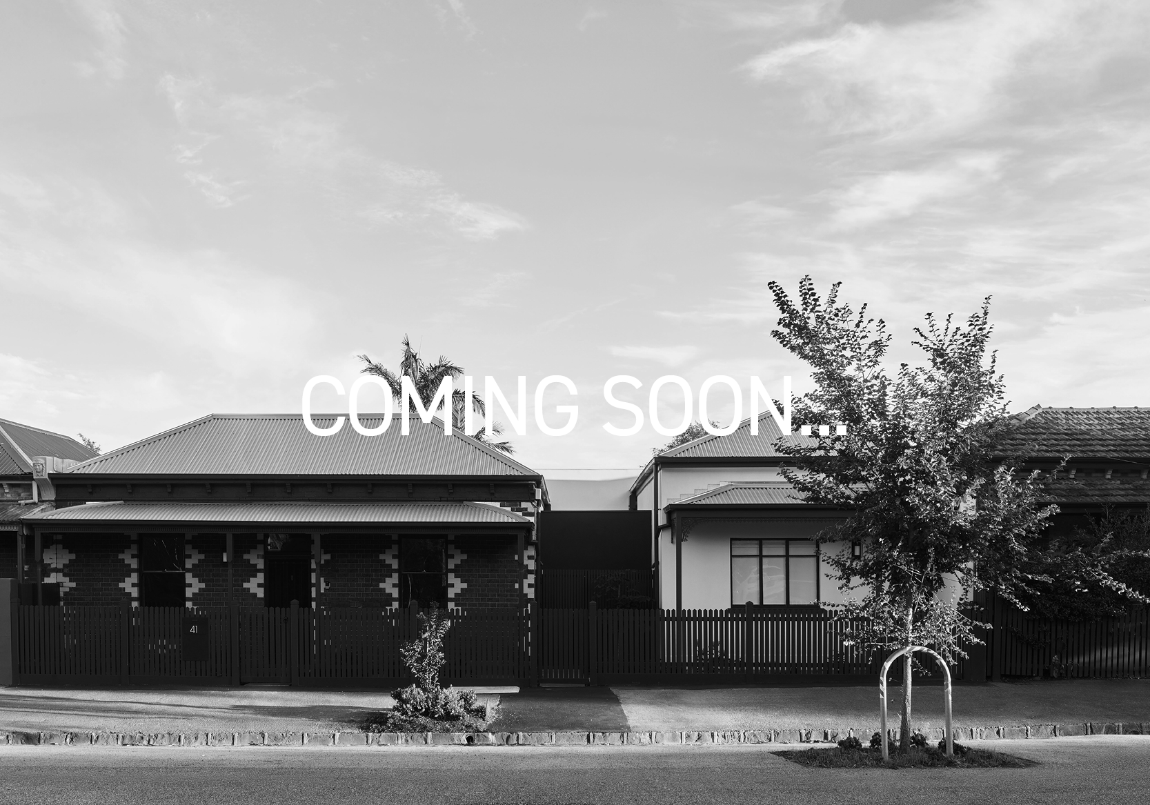 Black and white photo of suburban houses with trees in front, and the words 'Coming Soon...' written across the sky.