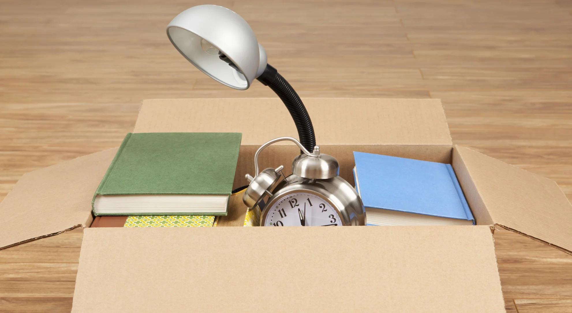 stacks-of-books-lamp-and-an-alarm-clock-in-a-cardboard-box-moving-house-or-garage-sale-items-2-1.jpg