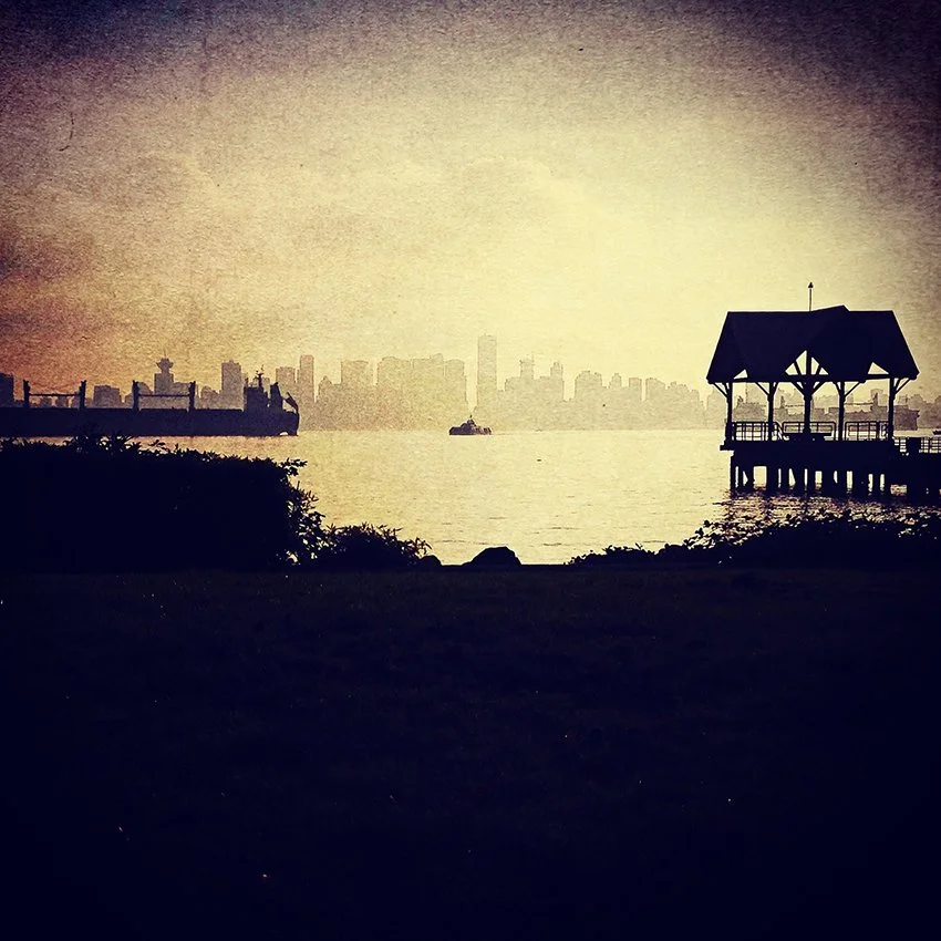 Silhouetted ship at anchor on the left, wooden shelter on a pier on right and small Seabus in the centre with foggy Vancouver skyline in the background.