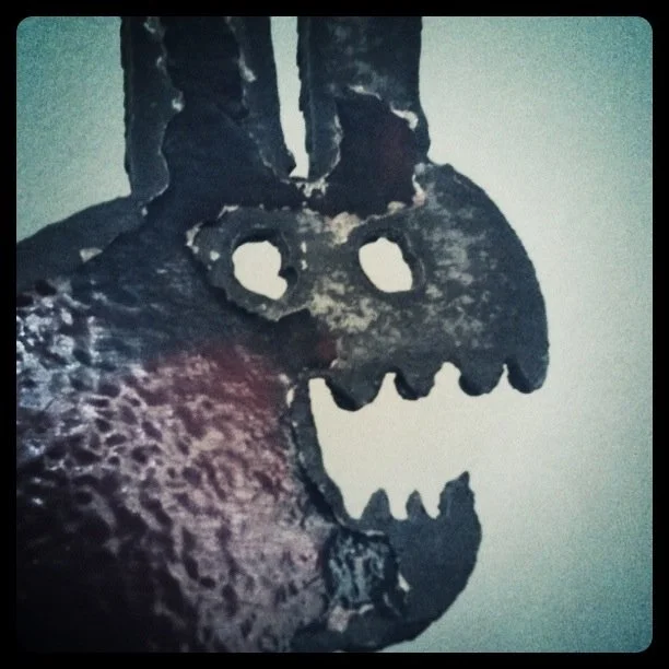 Close up of the head of a painted, distressed, steel rabbit sculpture with two holes for eyes and scary teeth.