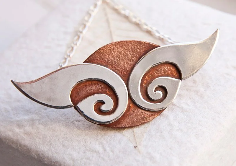 A pendant made of a copper oval with silver Celtic horn like elements extending beyond the copper and silver chain, made by Dana.