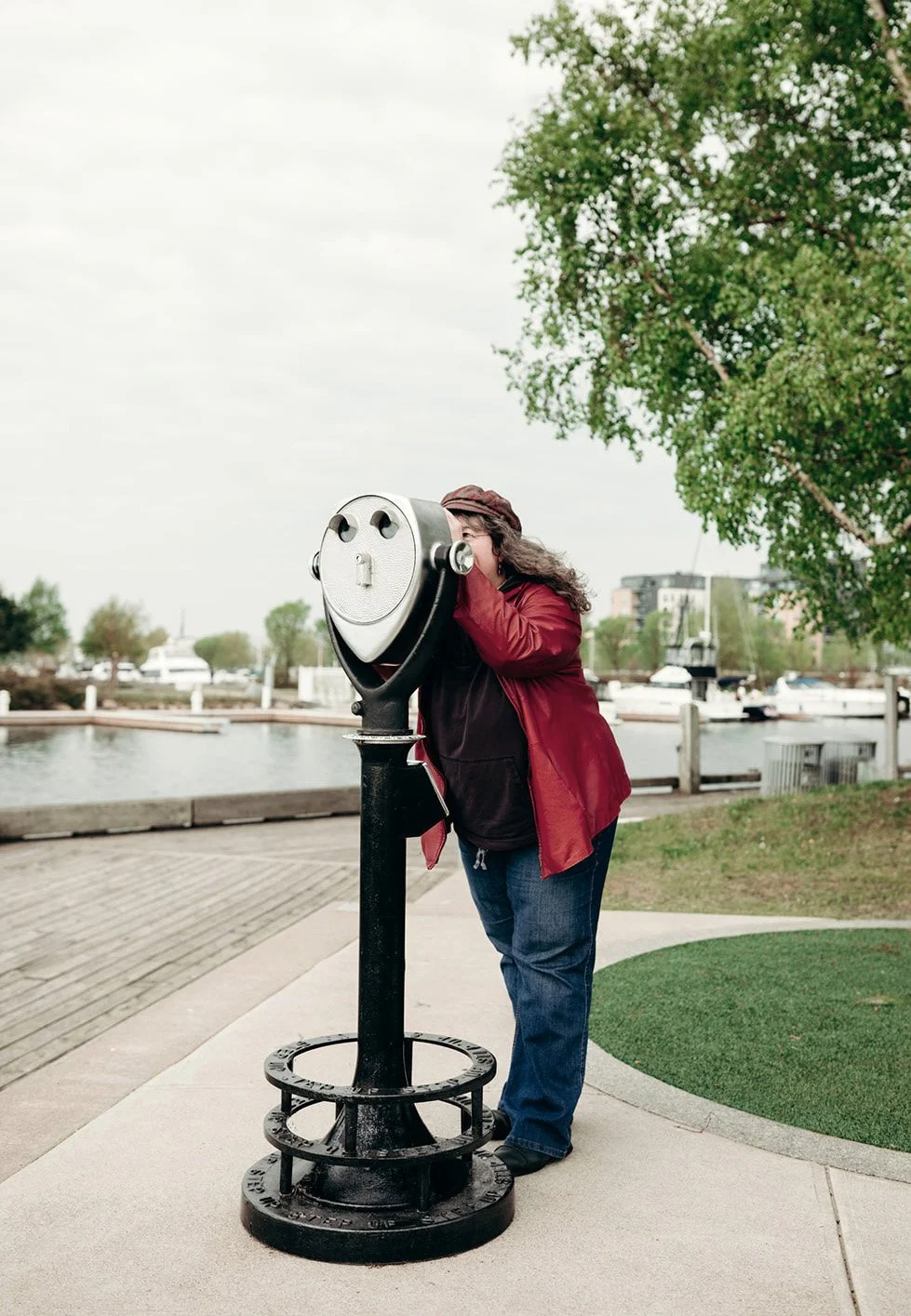 Dana, wearing red leather jacket and hat, looking through far-viewer at Thunder Bay marina.