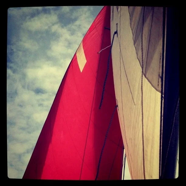 Red spinnaker sail against cloudy sky in background, taken from a sailboat cockpit.