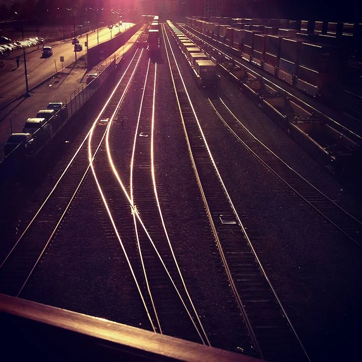 Dark brown image of North Vancouver rail yard with rail lines shining and sunlit, taken from the Seabus walkway.