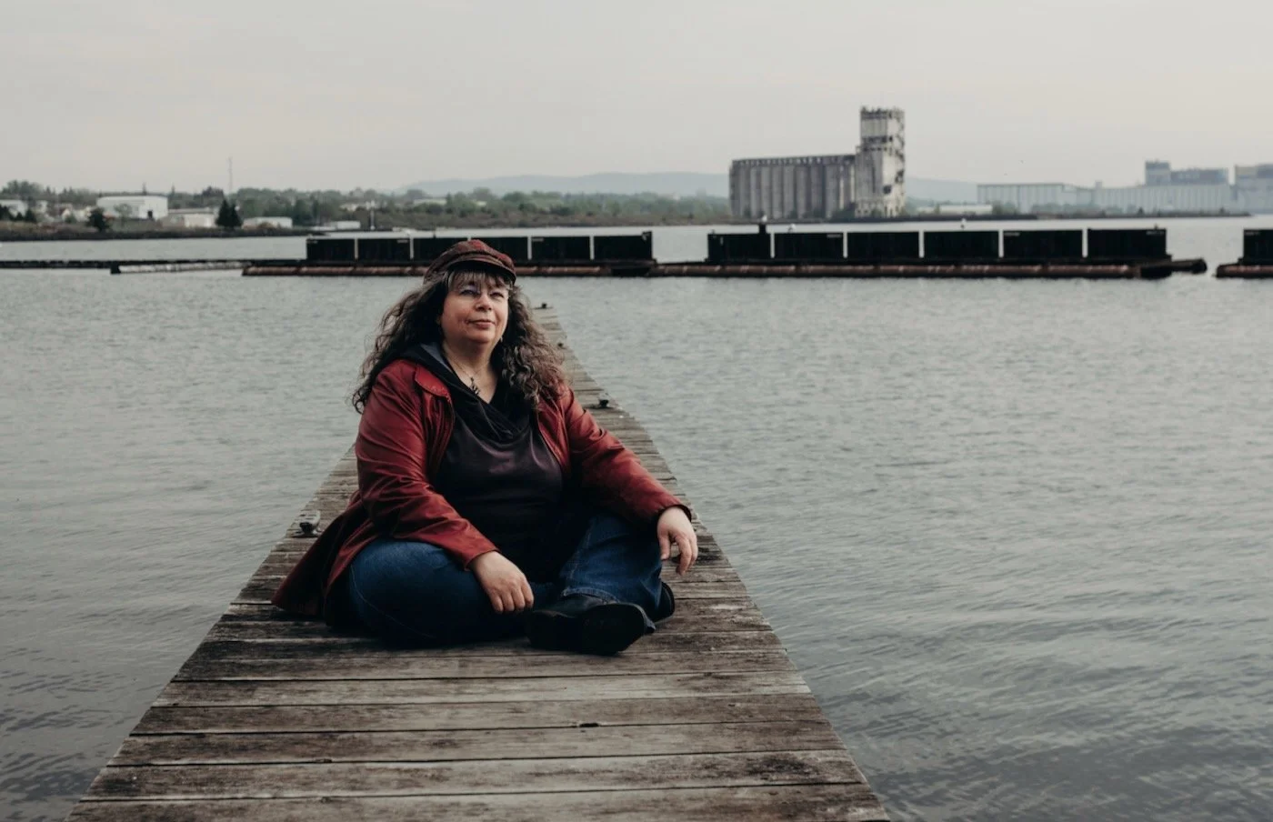 Web designer, Dana Reed, sitting on a dock at the Thunder Bay marina, in front of some grain elevators.