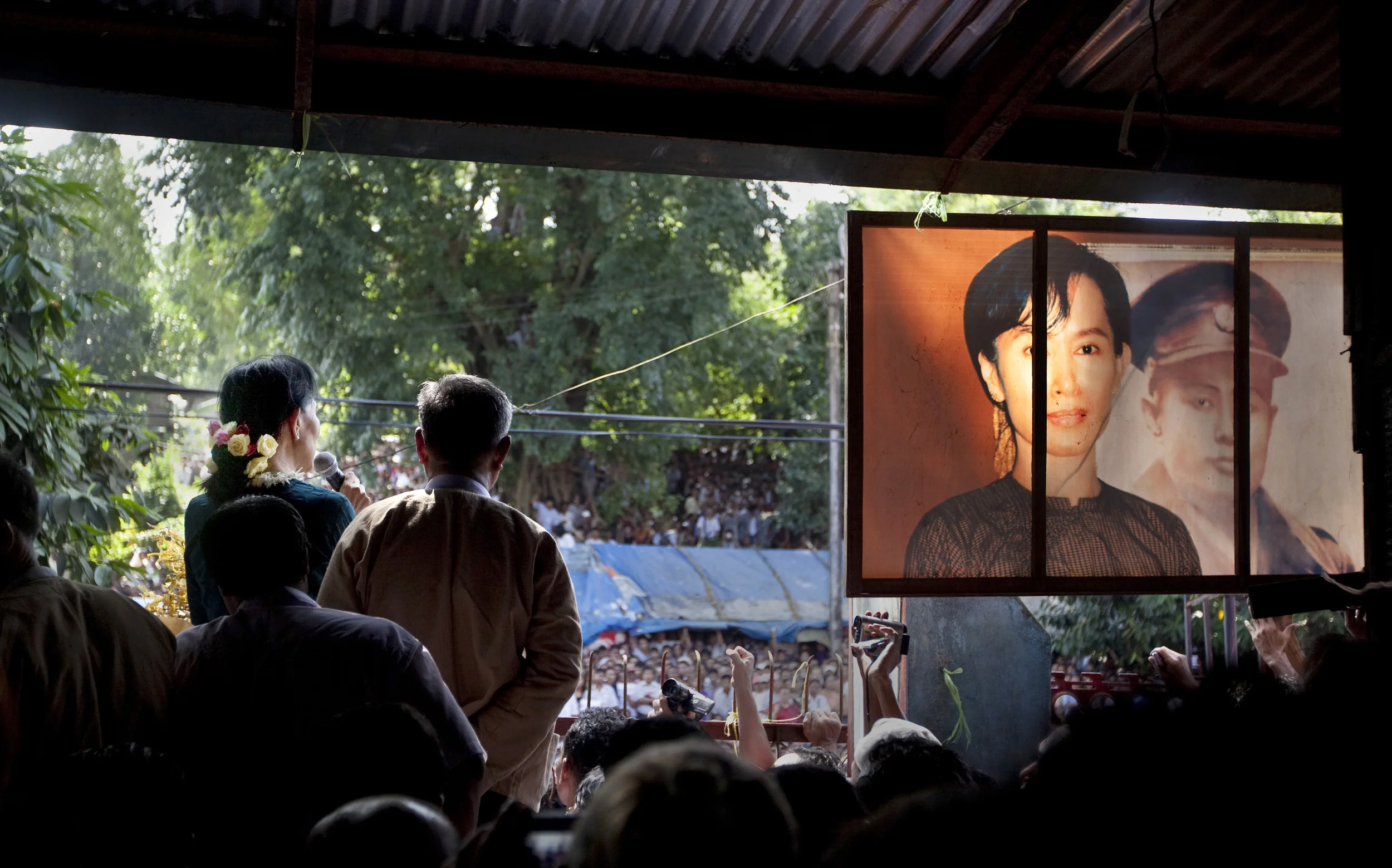 With her trademark floral hair-tie, Burma's Aung San Suu Kyi speaks to supporters in the days following her release from 15 years of house arrest. To he right a portrait of her next to her late father is on display. Rangoon, 2010.