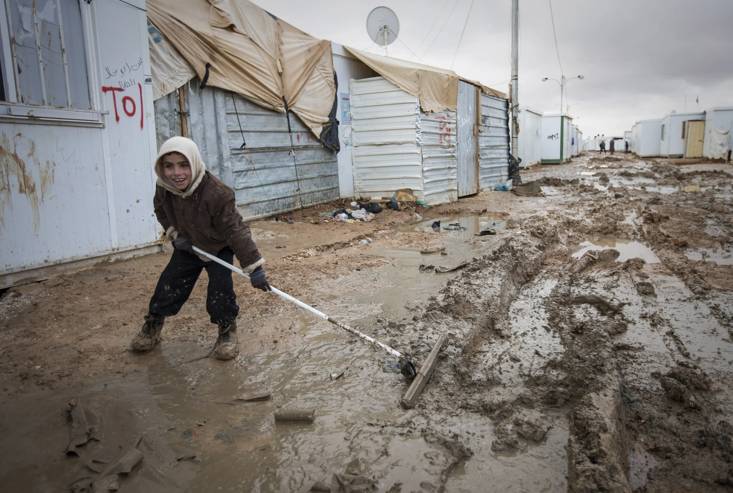 A young boy clears away mud and rainwater from his family, pre-fab dwelling at the Za'atari camp in Jordan where over 80,000 Syrian refugees are sheltering. December 2013.