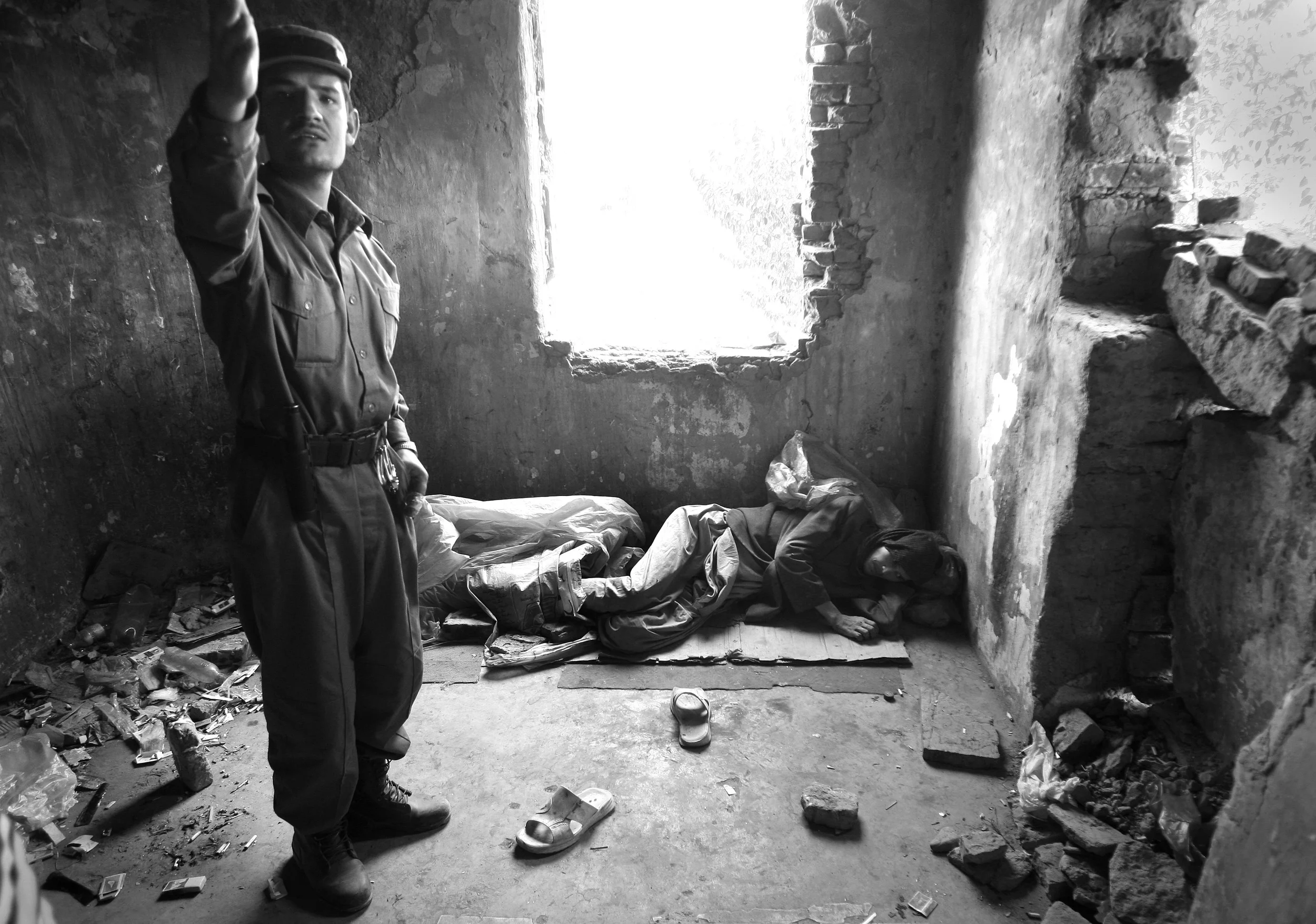  'Qossem', a heroin user of three years lies prostrate in the destroyed, former Russian Cultural Centre, a haven for drug addicts in Kabul, Afghanistan. The policeman stood by him, is there as a user and not on duty. &nbsp;September, 2009. 