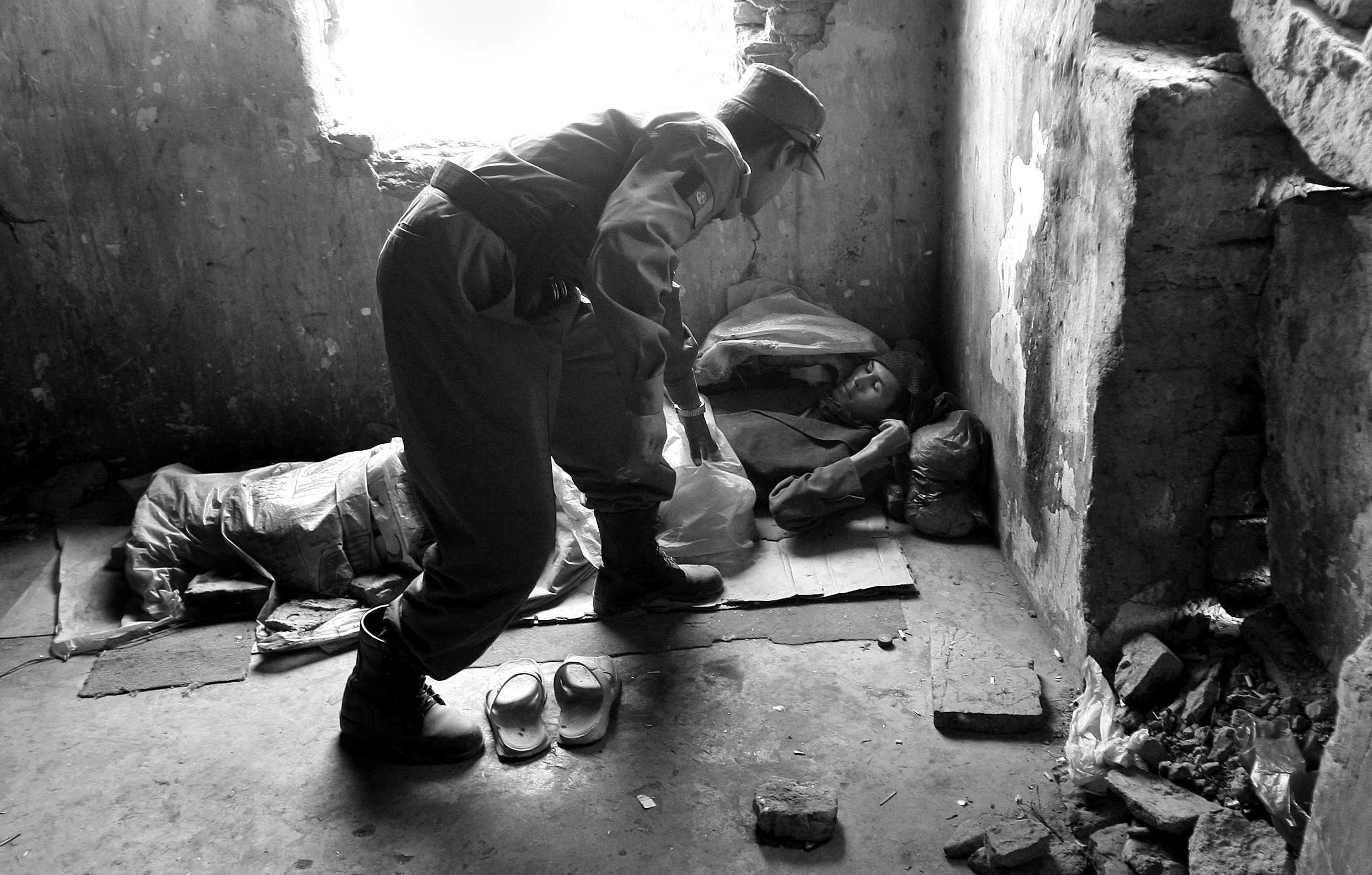  'Qossem', a heroin user of three years lies prostrate in the destroyed, former Russian Cultural Centre, a haven for drug addicts in Kabul, Afghanistan. The policeman, intervening, is there as a user and not on duty. &nbsp;September, 2009. 