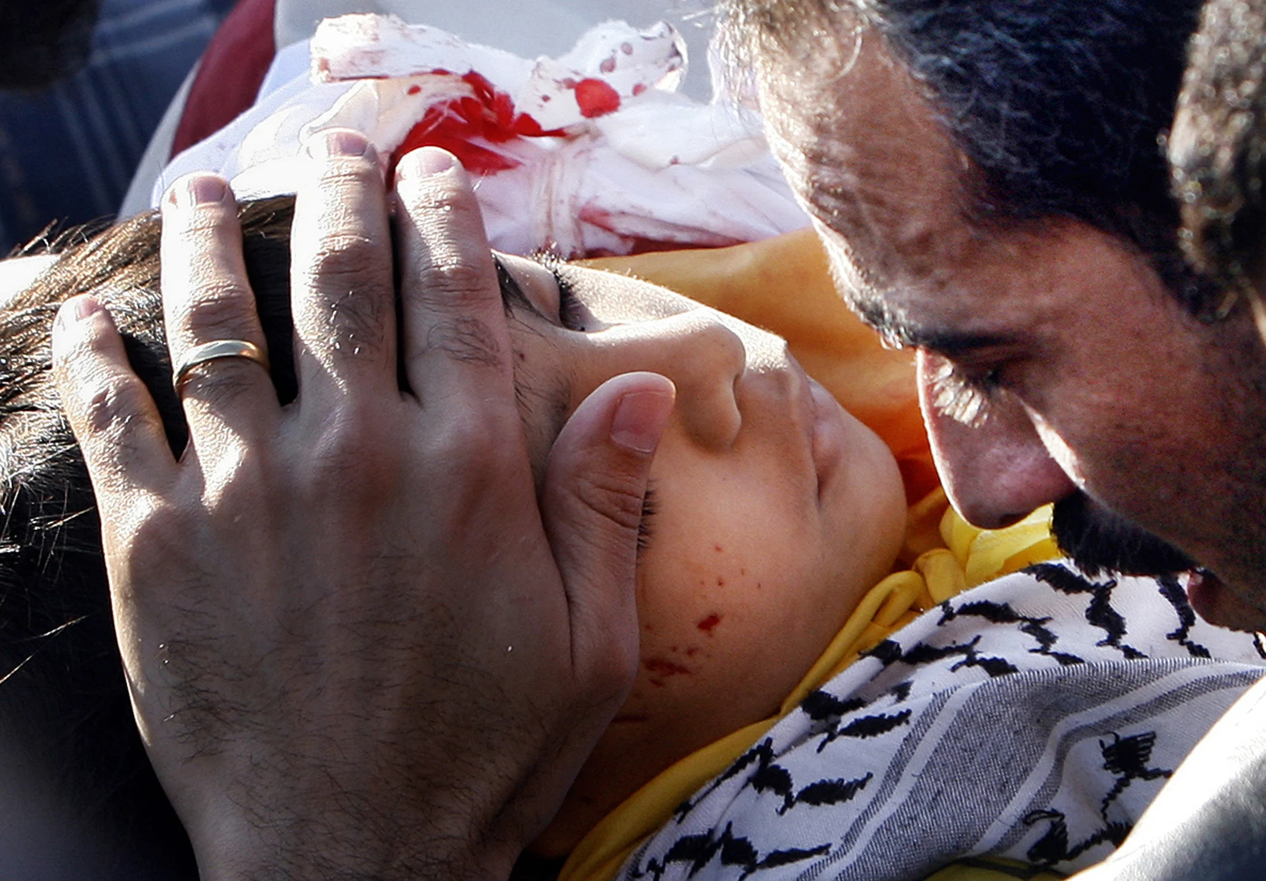 Palestinian security official Ba'aha Balousha, strokes the face of Osama, one of his three dead sons at their funeral, Monday, following their murder as they headed for school in Gaza city. December 2006.