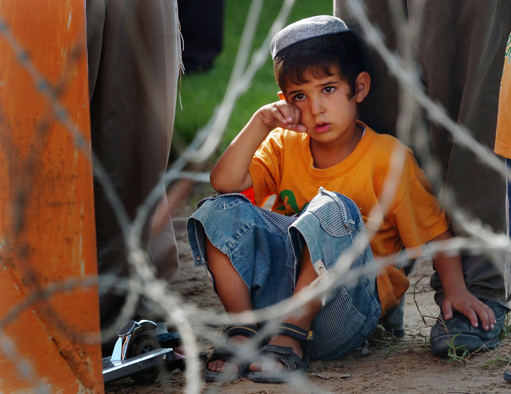  A child, by his settler fathers feet, sits behind razor wire in an attempt to deter police from removing them from their settlement in Gush Qatif, Gaza, as part of Israel's disengagement from the territory. &nbsp;August 2005. 