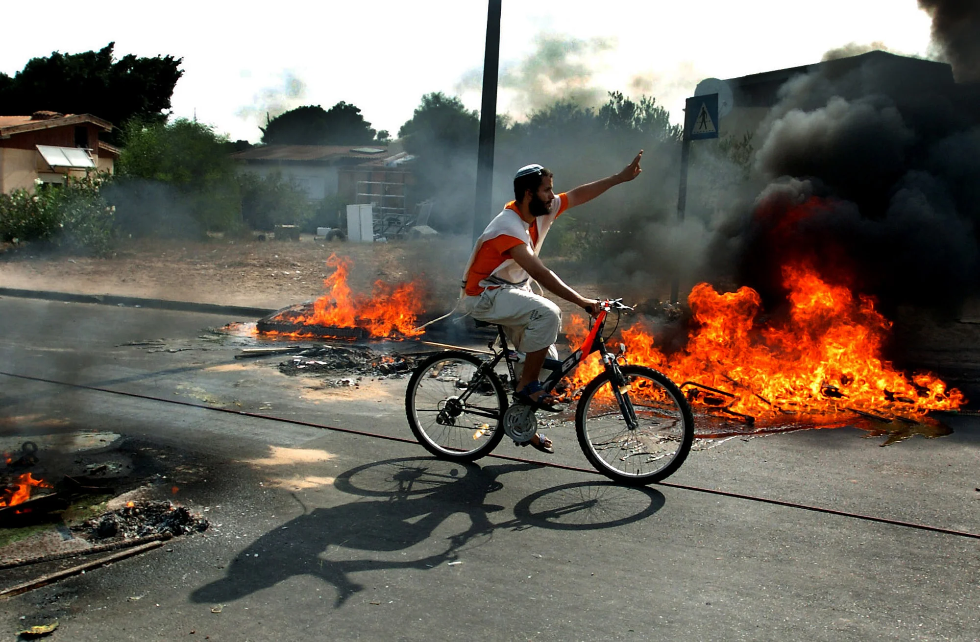  A defiant Israeli settler cycles through burning barricades in Newe Dekalim, Gaza, ahead of being forcibly removed by Israeli police as part of the disengagement. &nbsp;August 2005. 