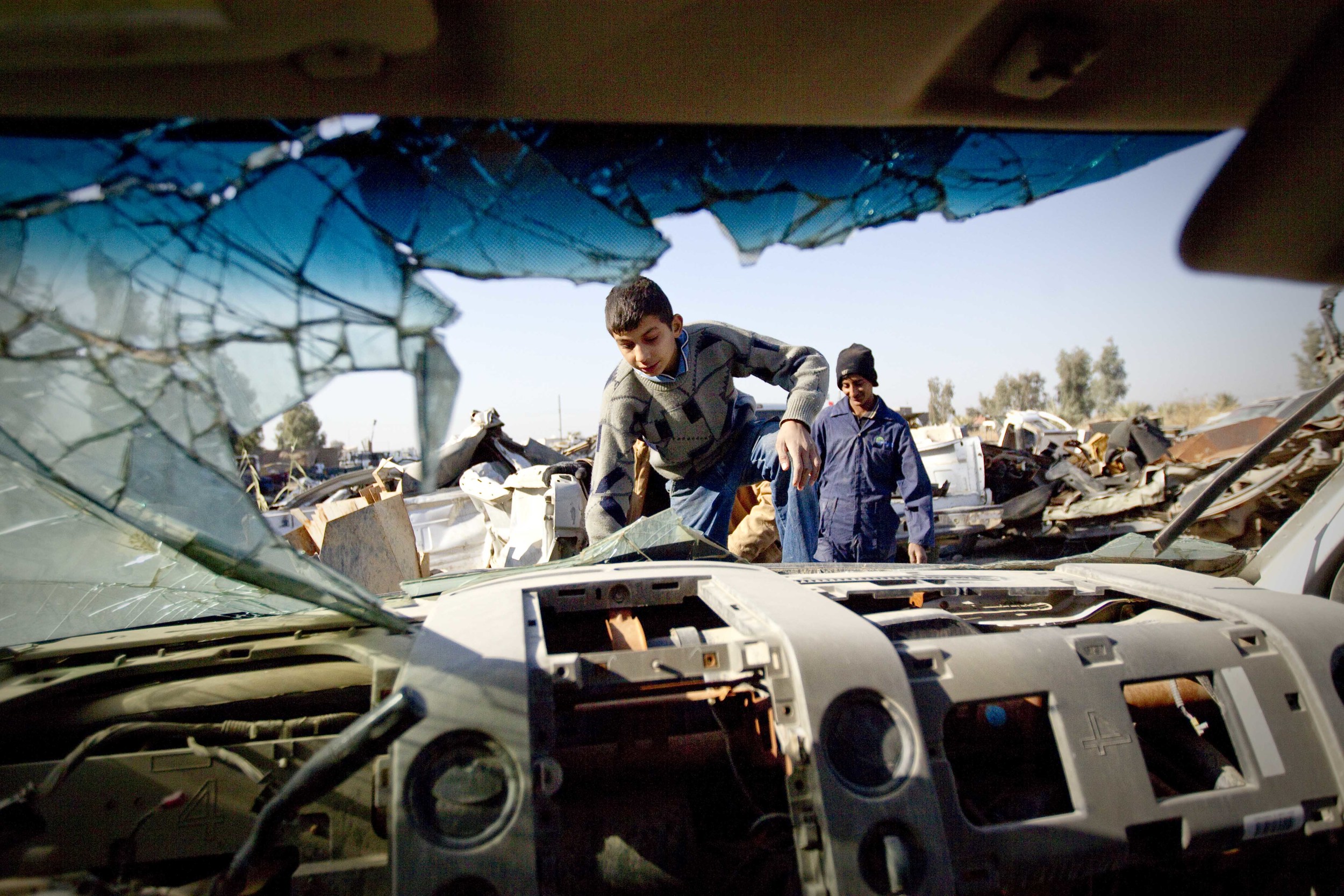  Teenage boys climb over discarded, American vehicles at a scrapyard full of 'salvaged' items from US bases near Taji, Iraq. December 2011. 