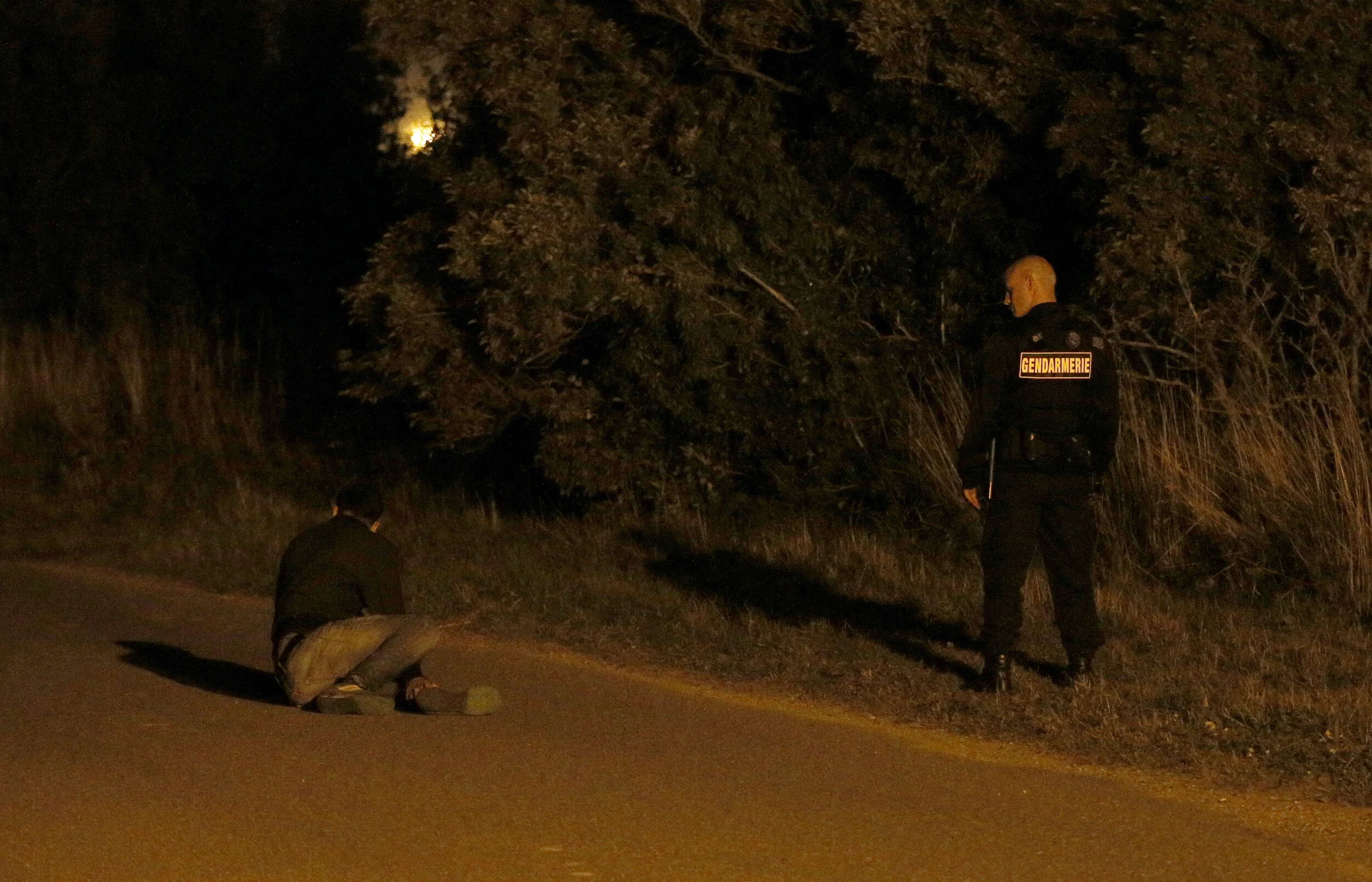  A French Gendarme talks with an injured migrant, lying on a road after he and several others were found hiding in bushes near to the entrance of the EuroTunnel in Calais, France, August 5, 2015 