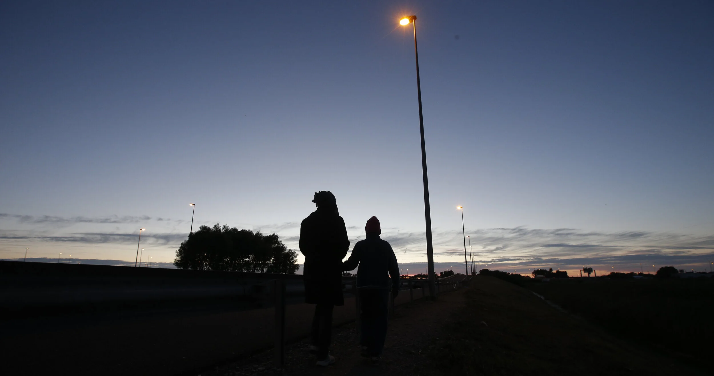 An Eritrean mother and her daughter are seen in silhouette as they walk along the motorway near the Channel Tunnel entrance near Calais, France, August 6, 2015 
