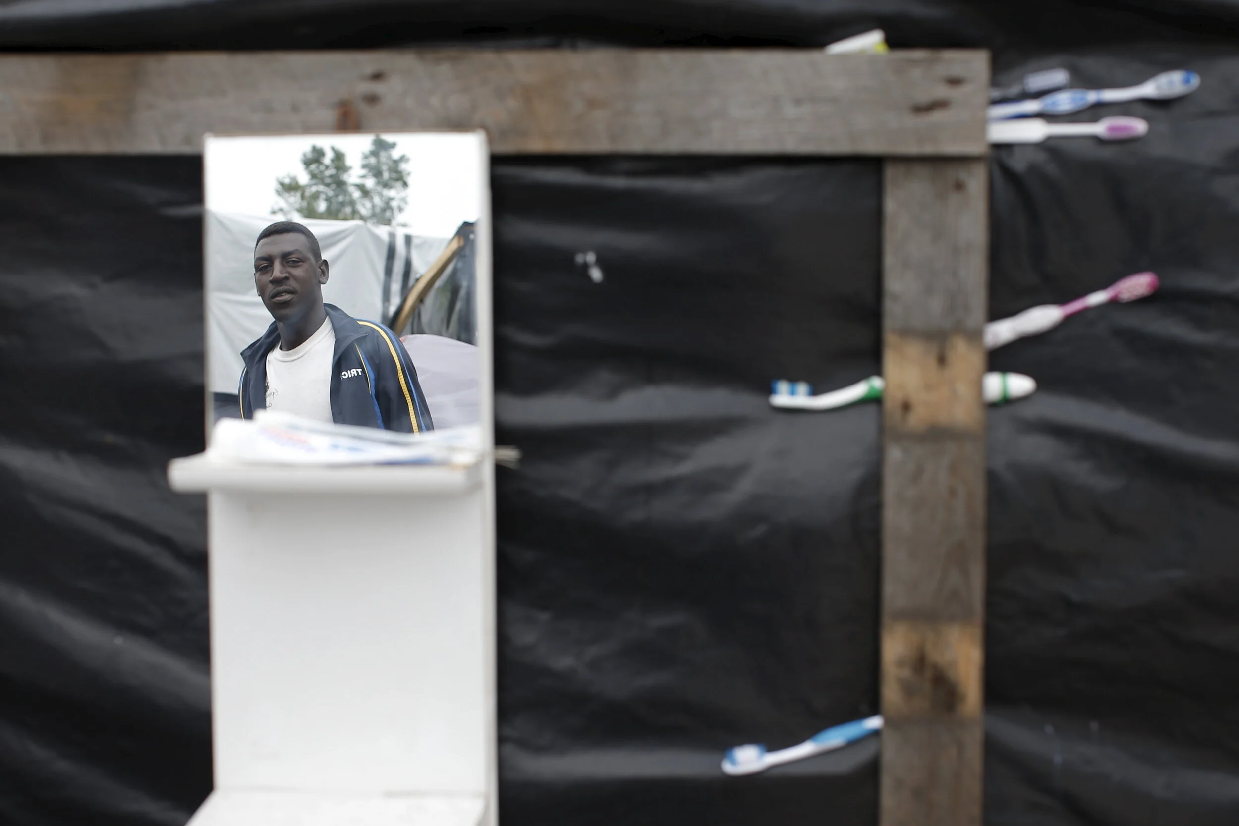  A migrant is reflected in a mirror attached to his temporary shelter at "The New Jungle" in Calais, France, August 6, 2015 