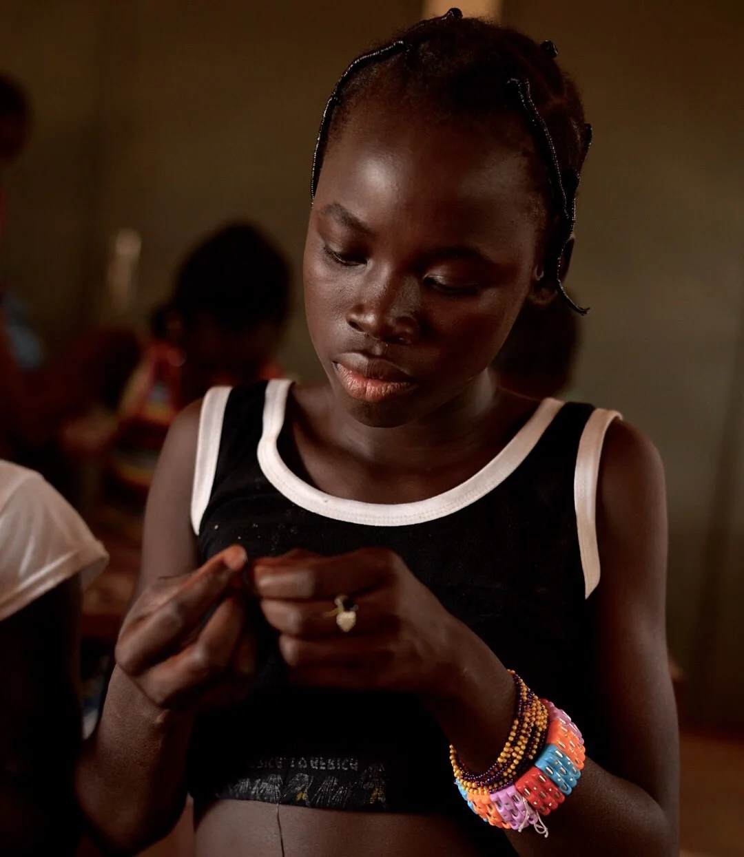Rosine studiously threads her bracelets.