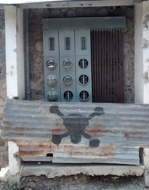 Electrical cables, panels and meters can be expensive to secure. Here the electric company warns you to stay away by using a piece of corrugated metal with a skull and cross bones painted on it.