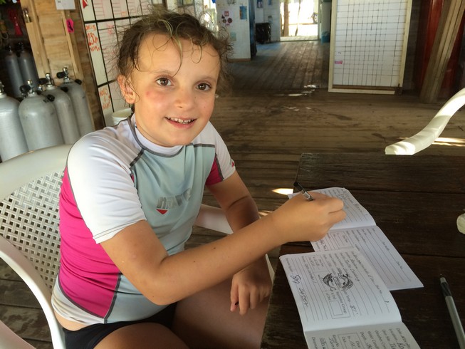 Ela completing her scuba diver book, recording the day's dive site, water temperatures and depth of dive. On this day, she also noted seeing an adult Hawksbill Sea Turtle . 