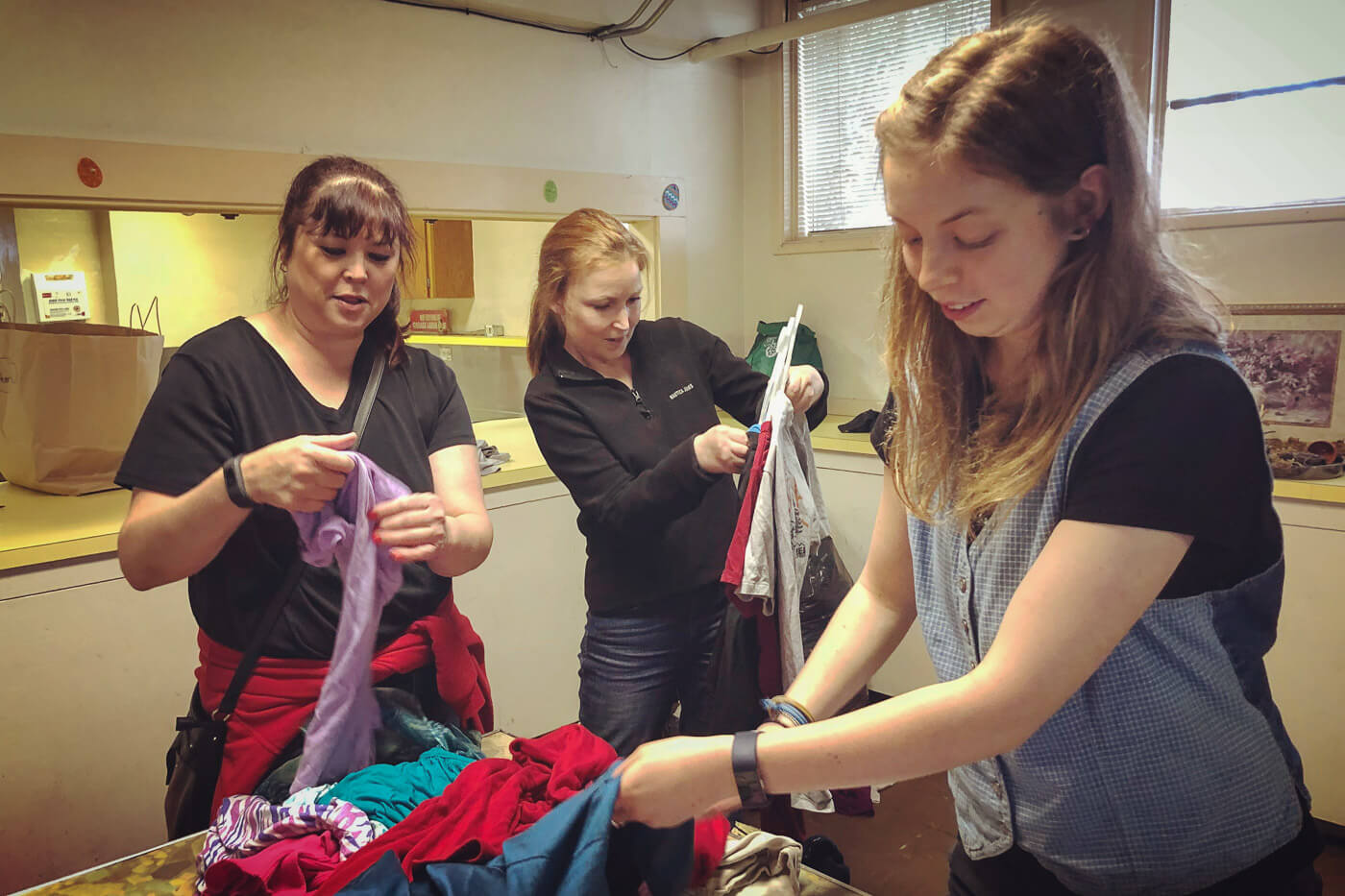 A trio of Friendly Exchange volunteers help sort and hang incoming clothing items so that you can get out there and shop for new threads faster.