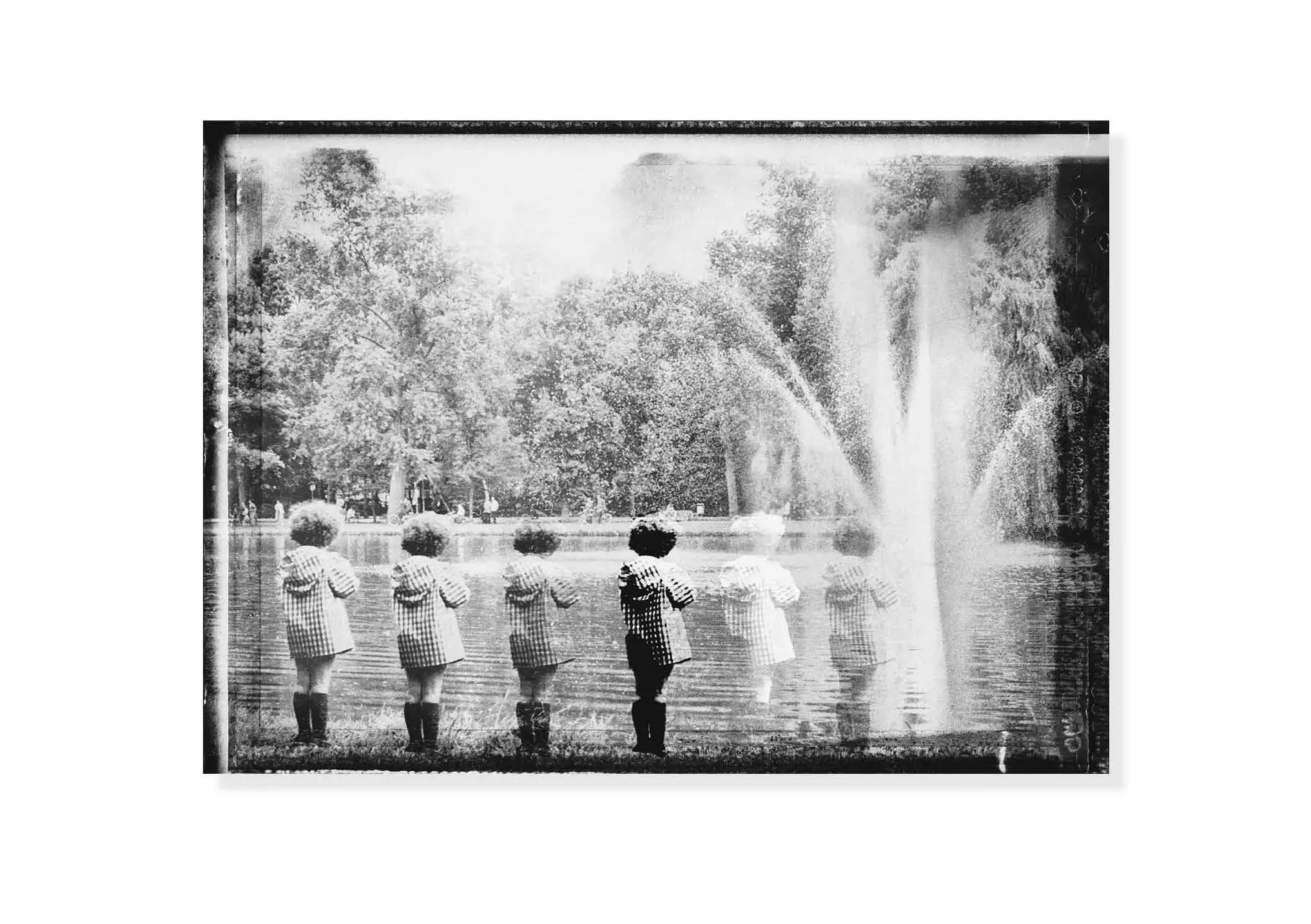 Black and white photo of children in striped outfits standing in a line facing a large fountain in a park.