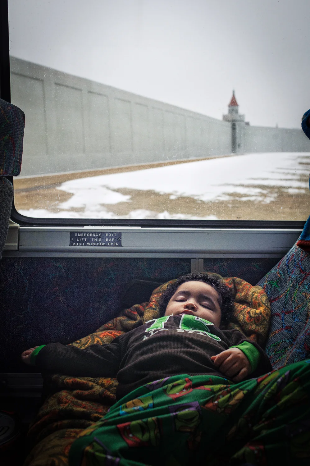 Jeremiah, 2, asleep as the bus is passing Attica prison in the early morning hours. Jeremiah is on his way to see his mother at Albion Correctional Facility. Albion is the largest women's prison in NY state, 20 miles from the Canadian Border. Jeremiah lives in the Bronx with his grandmother. March 8, 2014.