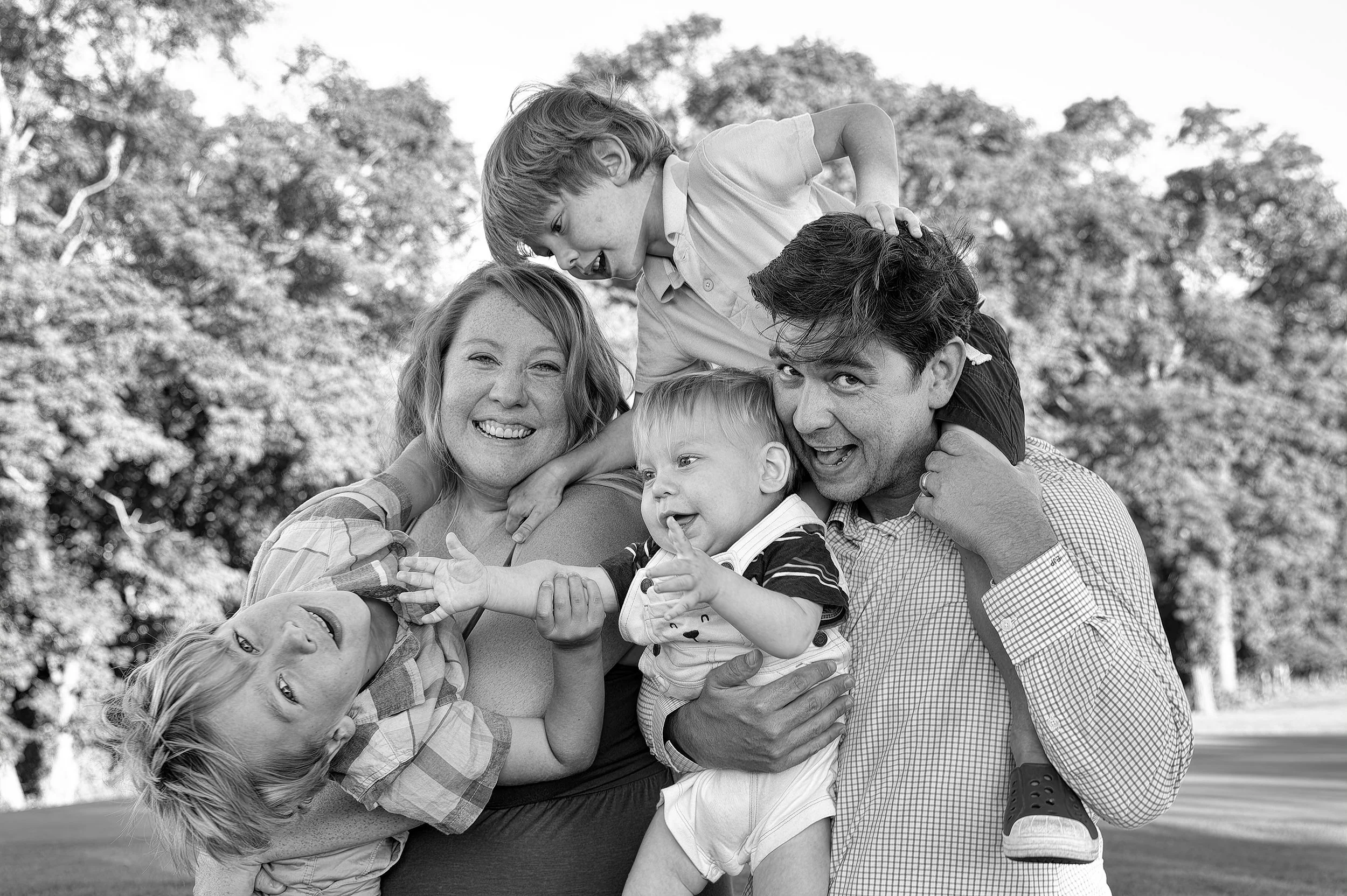 Black and white fun portrait of mom and dad with their three young energetic sons.